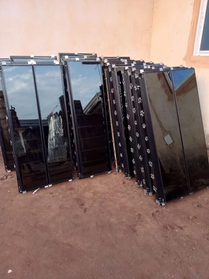 Plusieurs téléviseurs ou moniteurs noirs empilés contre un mur extérieur, certains reflètent le ciel et des bâtiments.