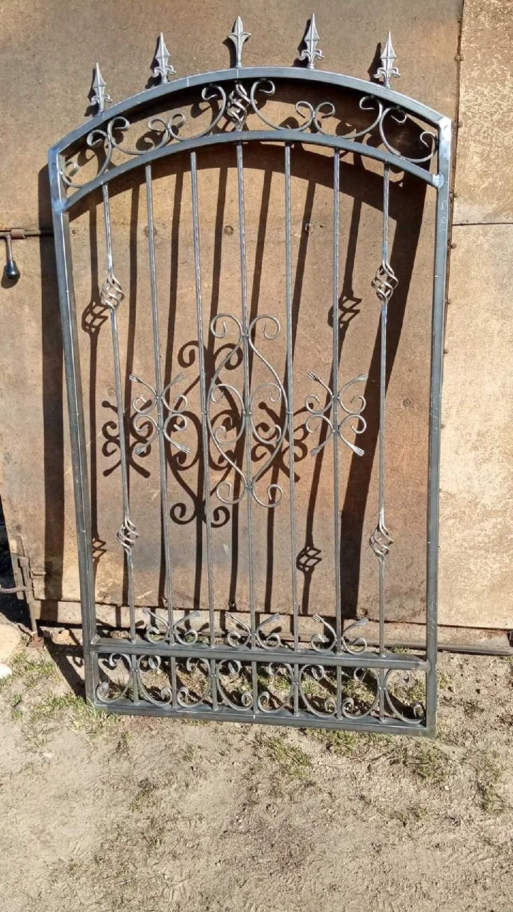 Une grille en métal noir avec des décorations florales et pointues, posée contre un mur en pierre.