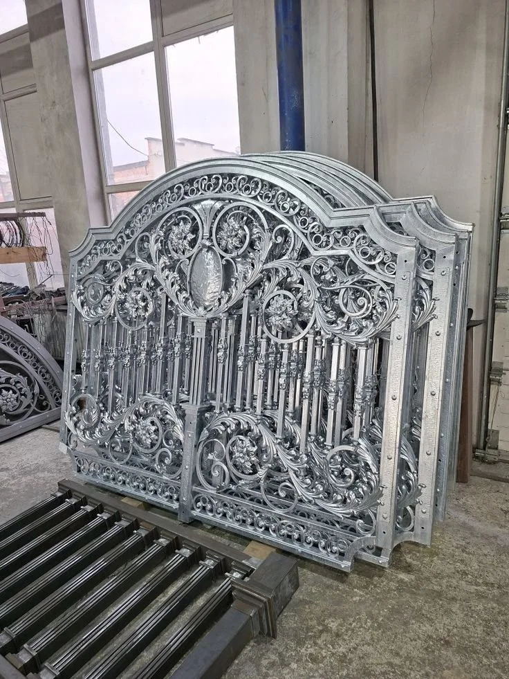 Une grille en métal finement travaillée avec des motifs ornementaux, probablement destinée à une porte ou une clôture, dans un atelier.