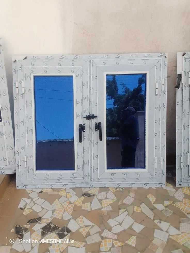 Fenêtre double avec cadre blanc, reflet d'une personne et du paysage extérieur, posé sur un sol en mosaïque.