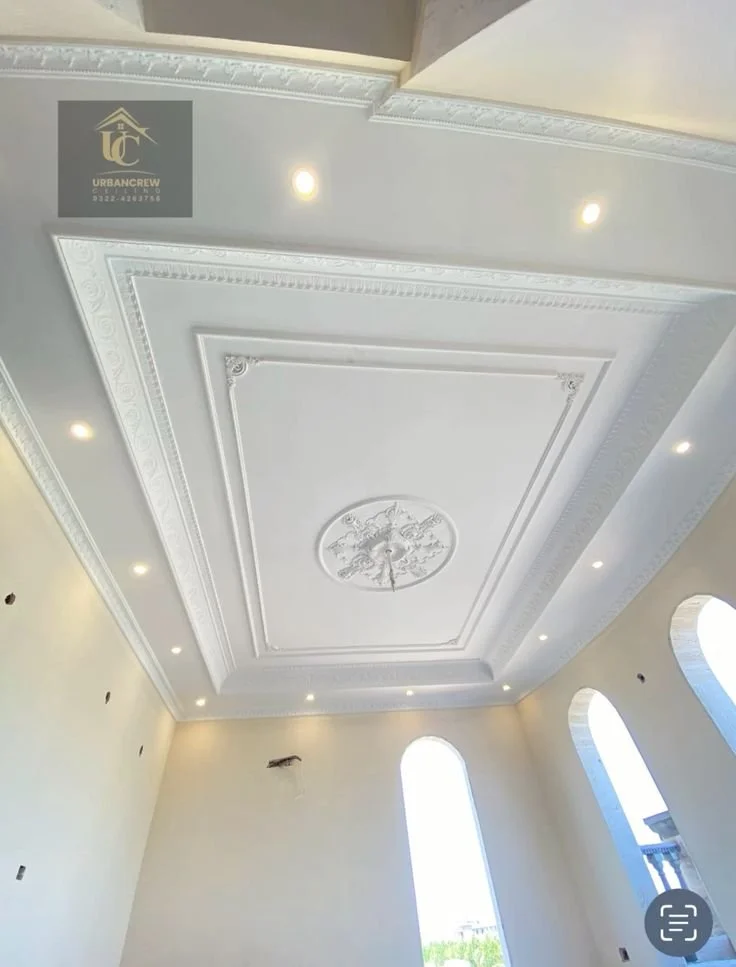 Plafond orné de moulures et d'une fresque centrale dans une pièce lumineuse avec des fenêtres en arches.