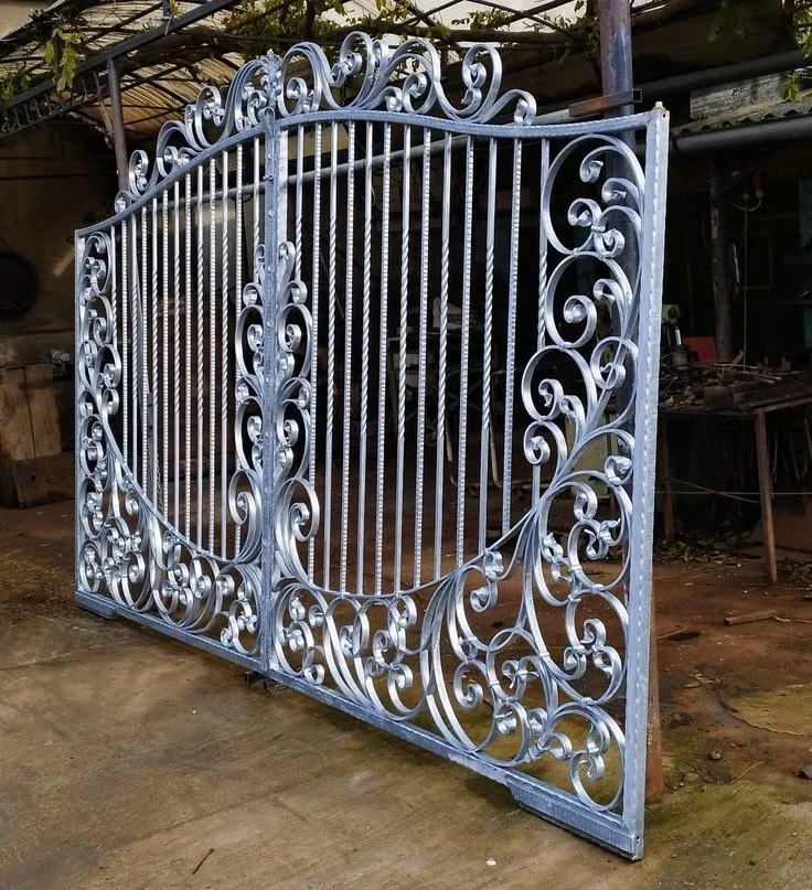 Une grille en fer ornée de motifs floraux et de spirales, posée en extérieur sur un sol en béton.