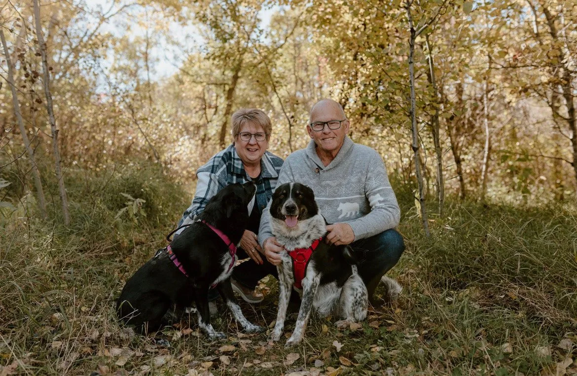 An elderly couple with two dogs adopted from ATTFR in a wooded area during autumn.
