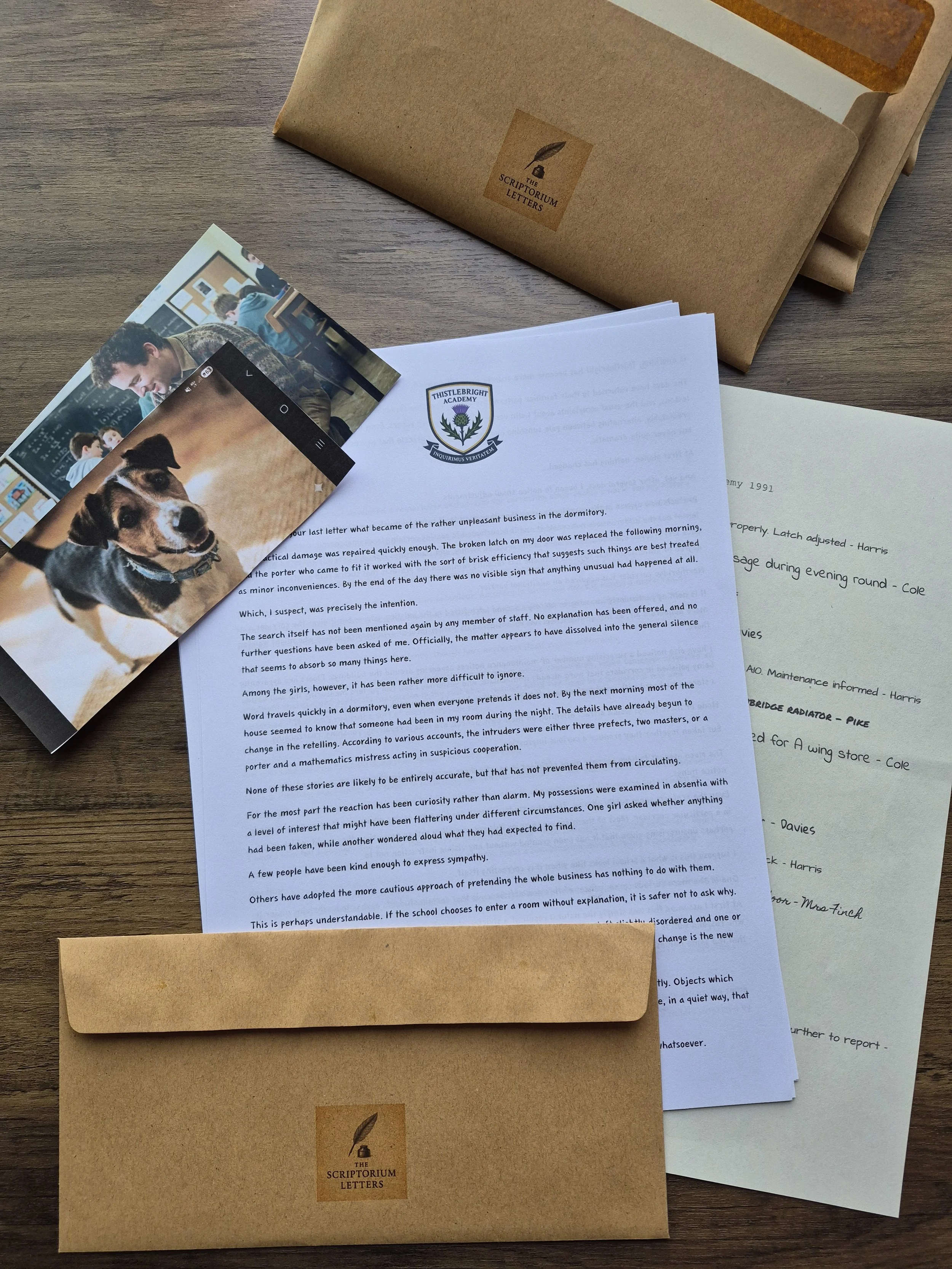 A collection of letters, photographs, and envelopes on a wooden table. The letters are printed with a crest reading 'Thistlebright Academy' with a thistle emblem, and some envelopes are labeled 'The Scriptorium Letters' with a quill pen illustration.