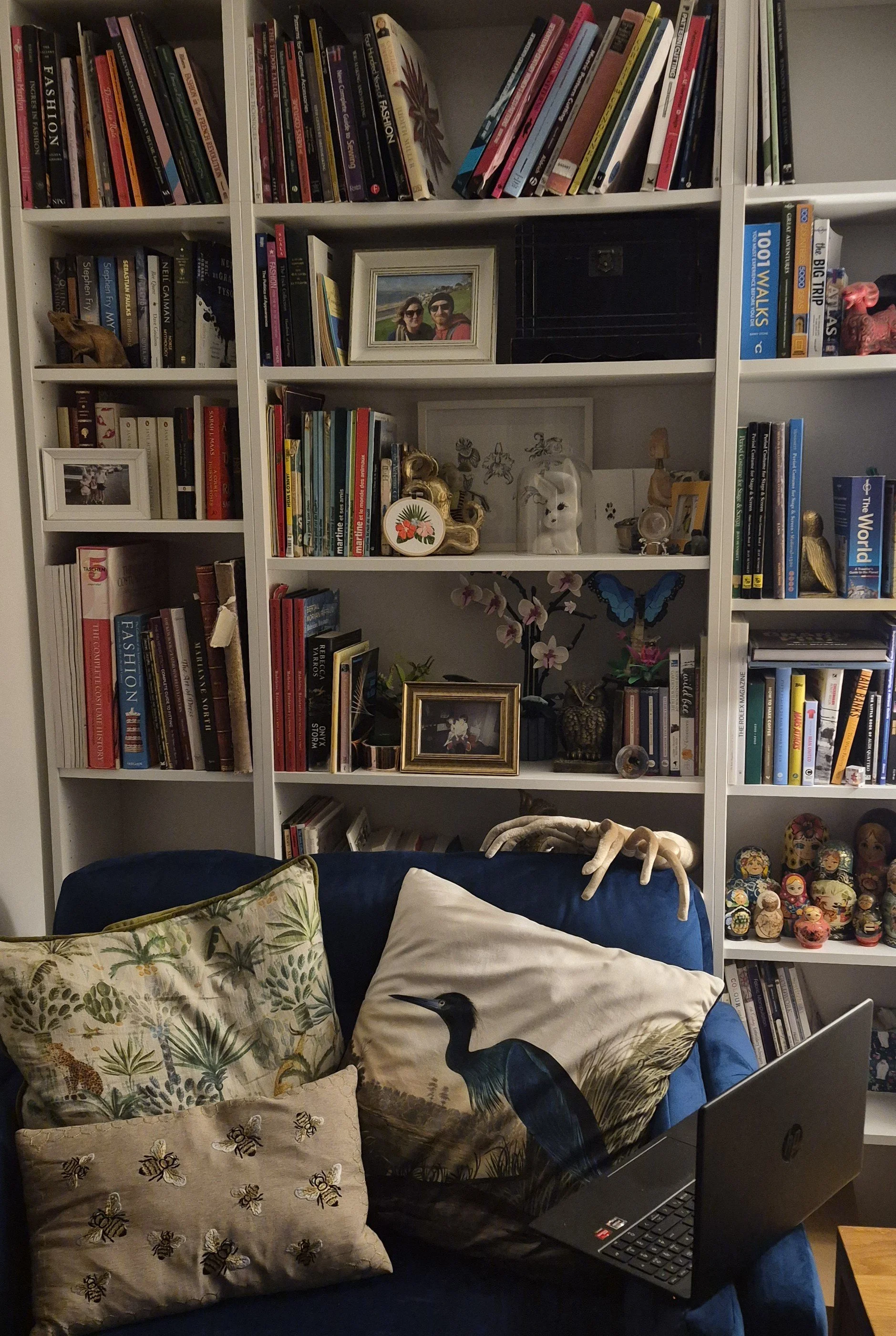 Living room with white bookshelves filled with books, framed photographs, and decorative items, and a blue couch with pillows, a laptop, and animal-shaped decor.