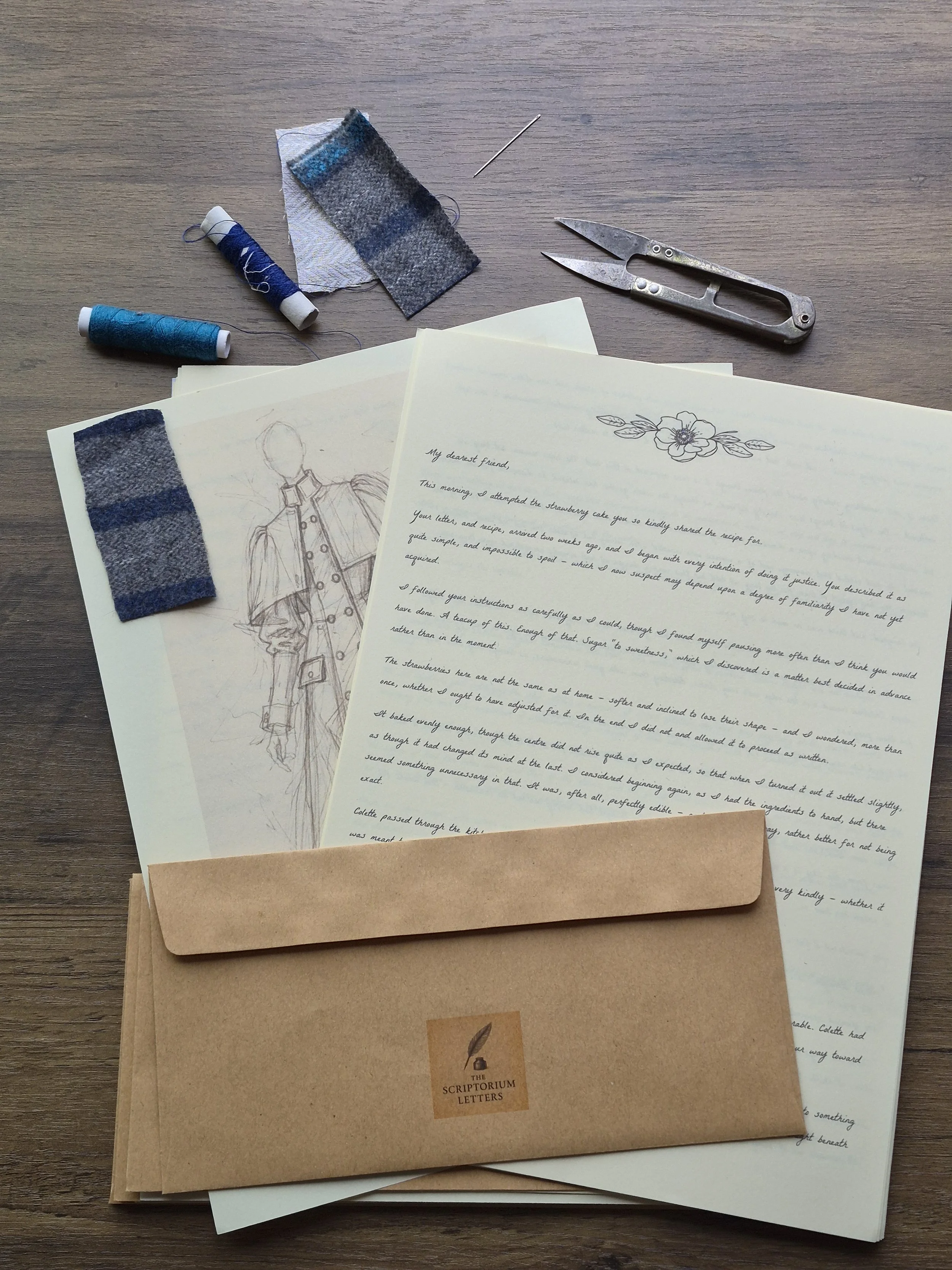 A collection of papers, fabric swatches, sewing needles, and thread spools on a wooden surface. The papers include handwritten letters and sketches, and a brown envelope labeled 'The Scripturium Letters'.