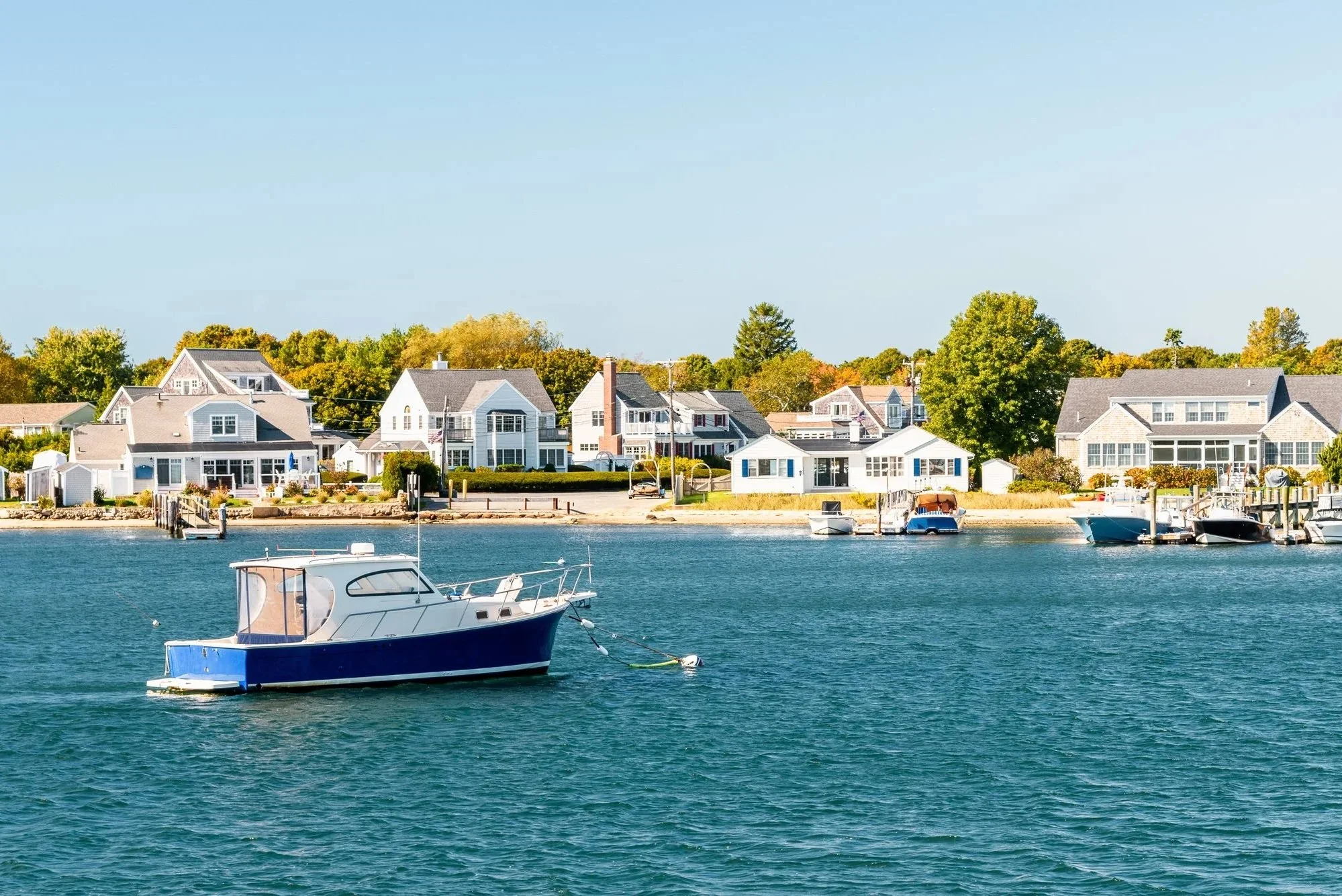 View of a waterfront residential area with colorful houses and boats anchored in the water under a clear blue sky.