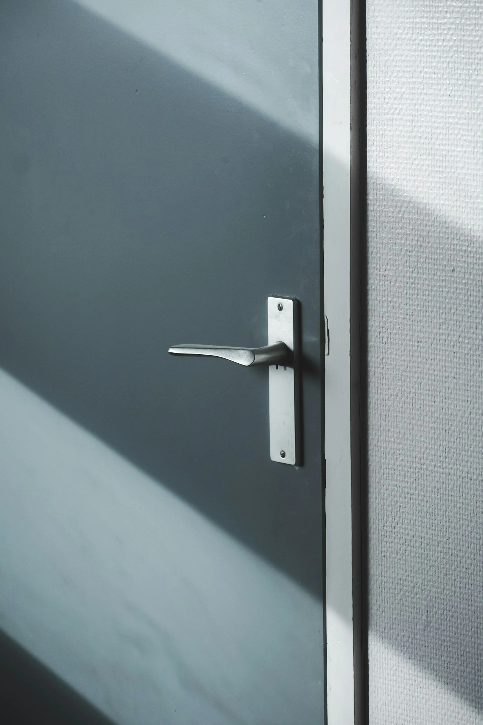 A closed gray door with a silver handle, adjacent to a textured white wall.