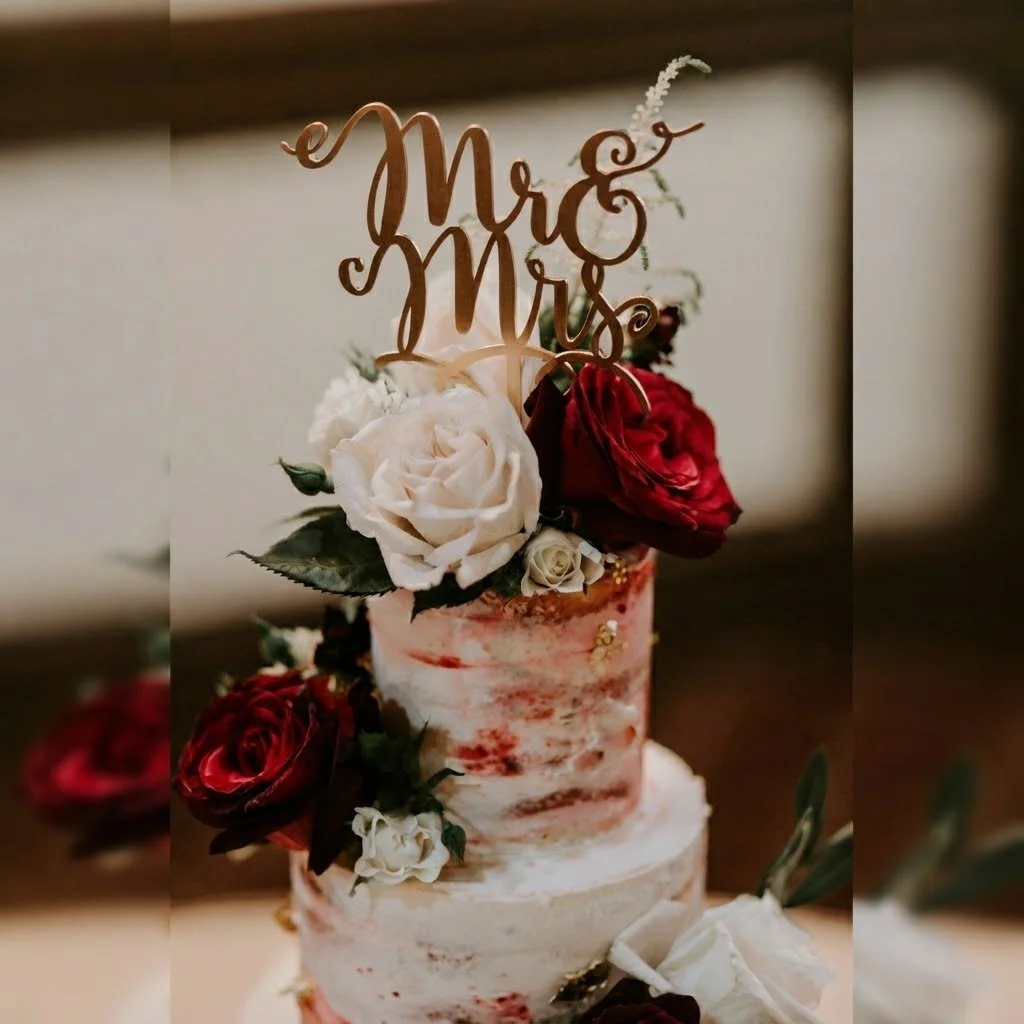 Elegant two-tiered wedding cake decorated with classic red and white roses and gold topper. Handcrafted luxury wedding cakes for romantic celebrations.
