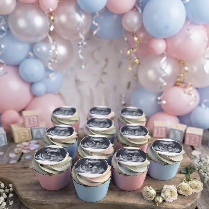 Pastel coloured ultrasound cupcakes for a gender reveal party on a wooden board with balloons. Handcrafted bespoke treats for memorable celebrations.