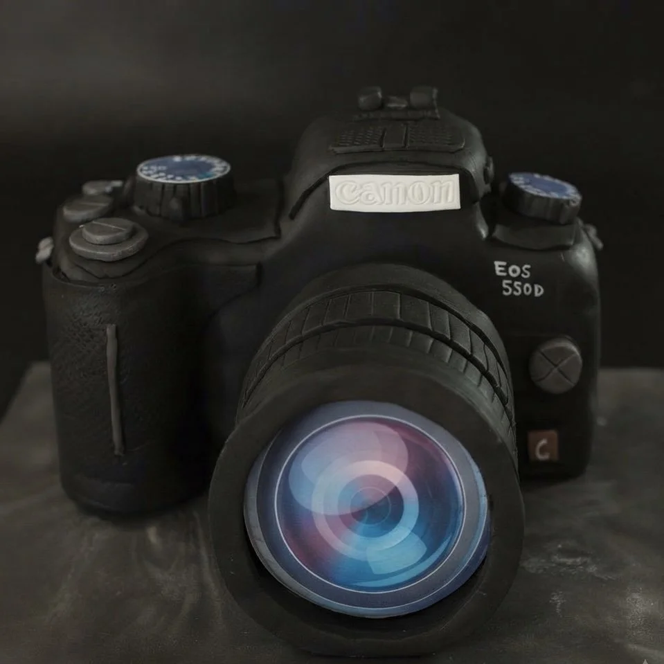 A black Canon EOS 550D camera with a large lens on a dark surface.