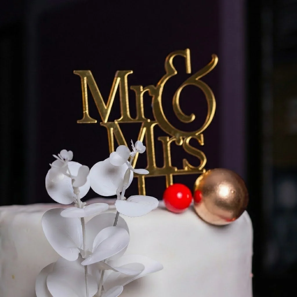 Elegant white iced wedding cake decorated with white orchids, red berries, and gold accents. Handcrafted luxury wedding cakes for romantic celebrations.