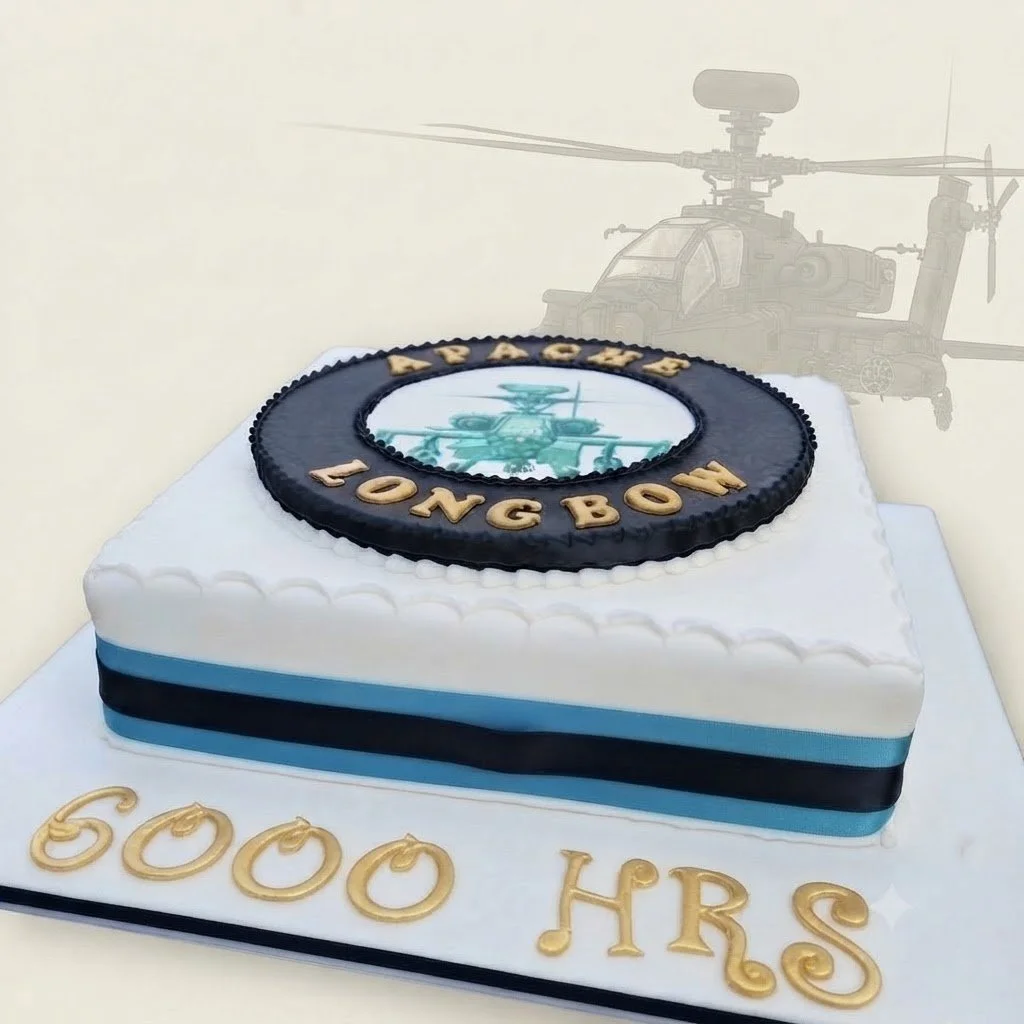 Square cake with white, black and blue icing, decorated with an Apache Longbow helicopter emblem and gold lettering reading “APACHE LONG BOW” and “6000 HRS.”
