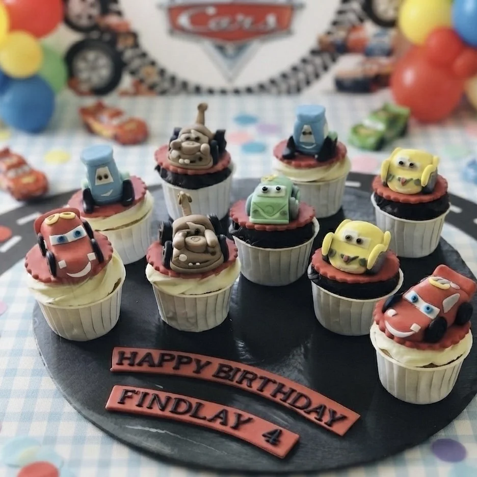 Fun animated Cars movie themed cupcakes on a black tray with a birthday message for a party. Handcrafted bespoke treats made for children's events.