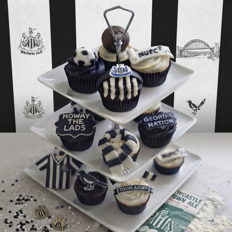 Newcastle United themed cupcakes with black and white icing on a three-tier stand with memorabilia. Handcrafted bespoke treats for football fans.