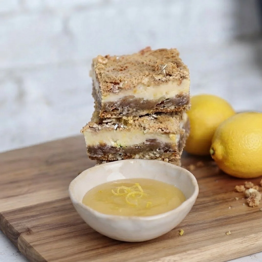 Decadent stack of two lemon bars served with fresh lemon curd on a wooden cutting board. Handcrafted luxury treats designed for sweet indulgence.