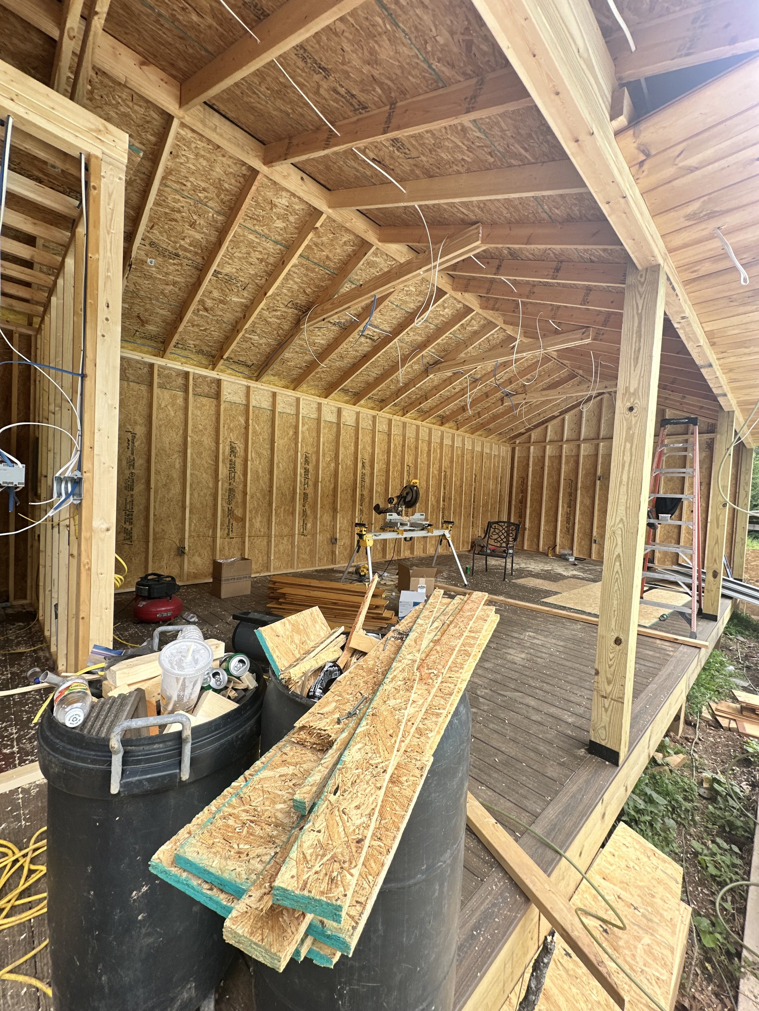 Construction site with unfinished wooden framing, scattered wood planks, a ladder, buckets, and tools.