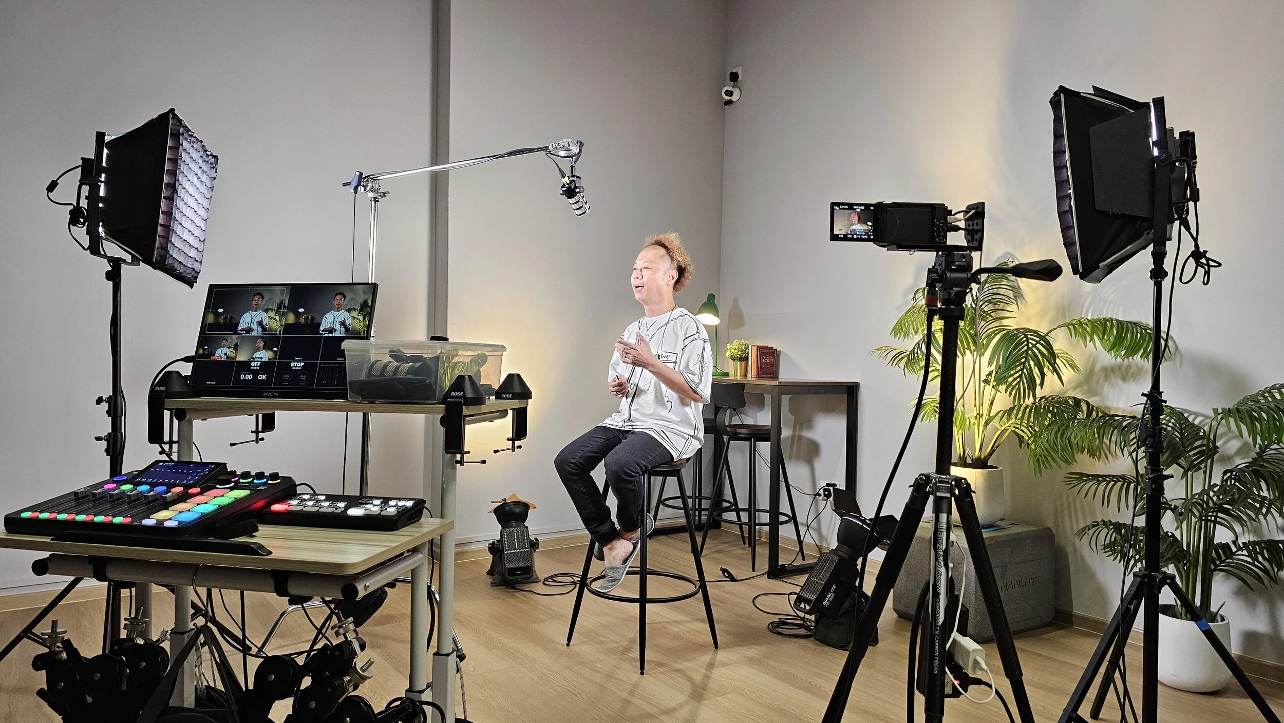 Jason Elpheus Wong, sitting on a stool in Gratias Studio with camera equipment, lights, and podcast equipment, doing a test shoot.