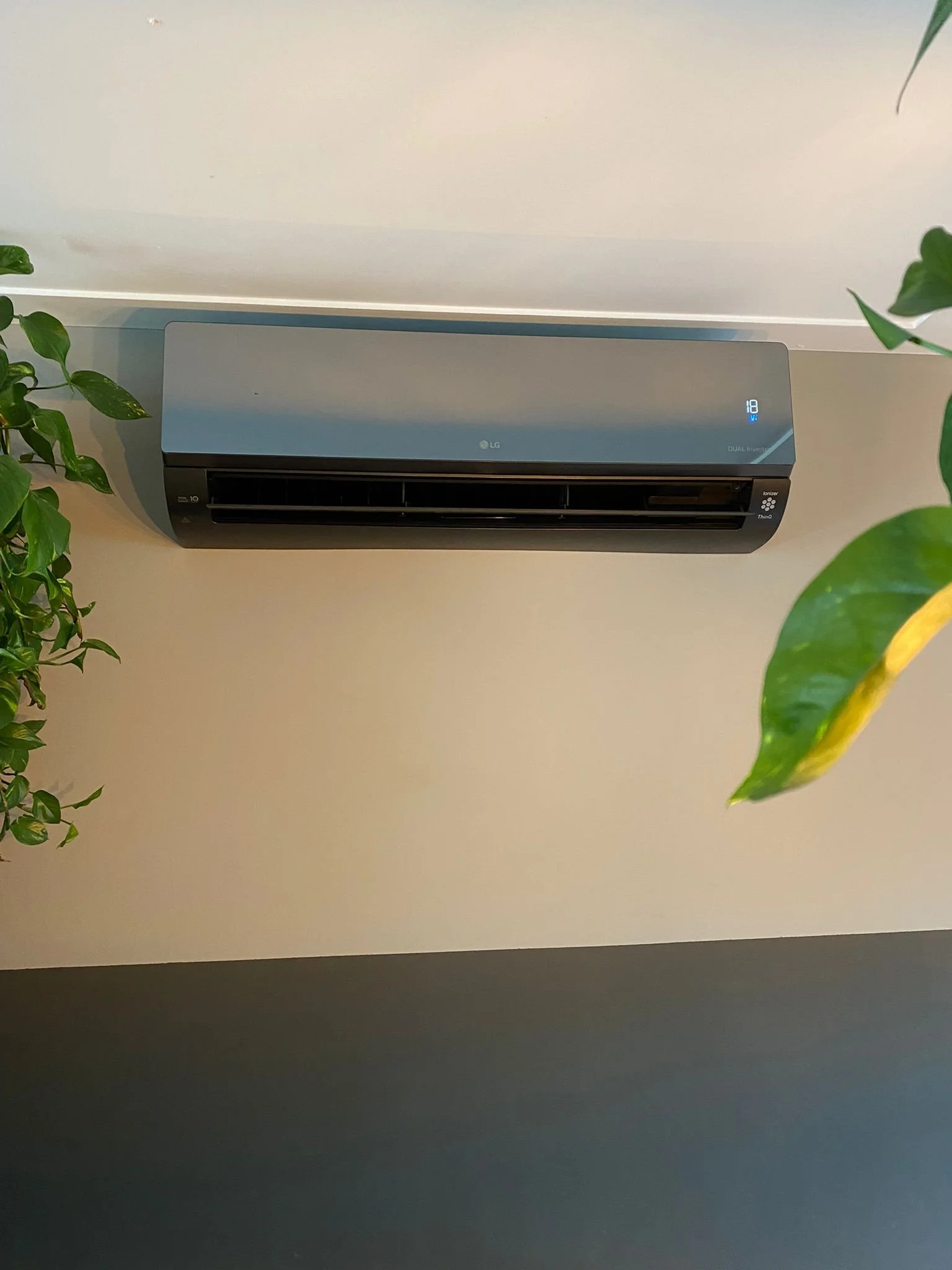 Vloer airconditioning unit met groene planten eromheen aan het plafond bevestigd.