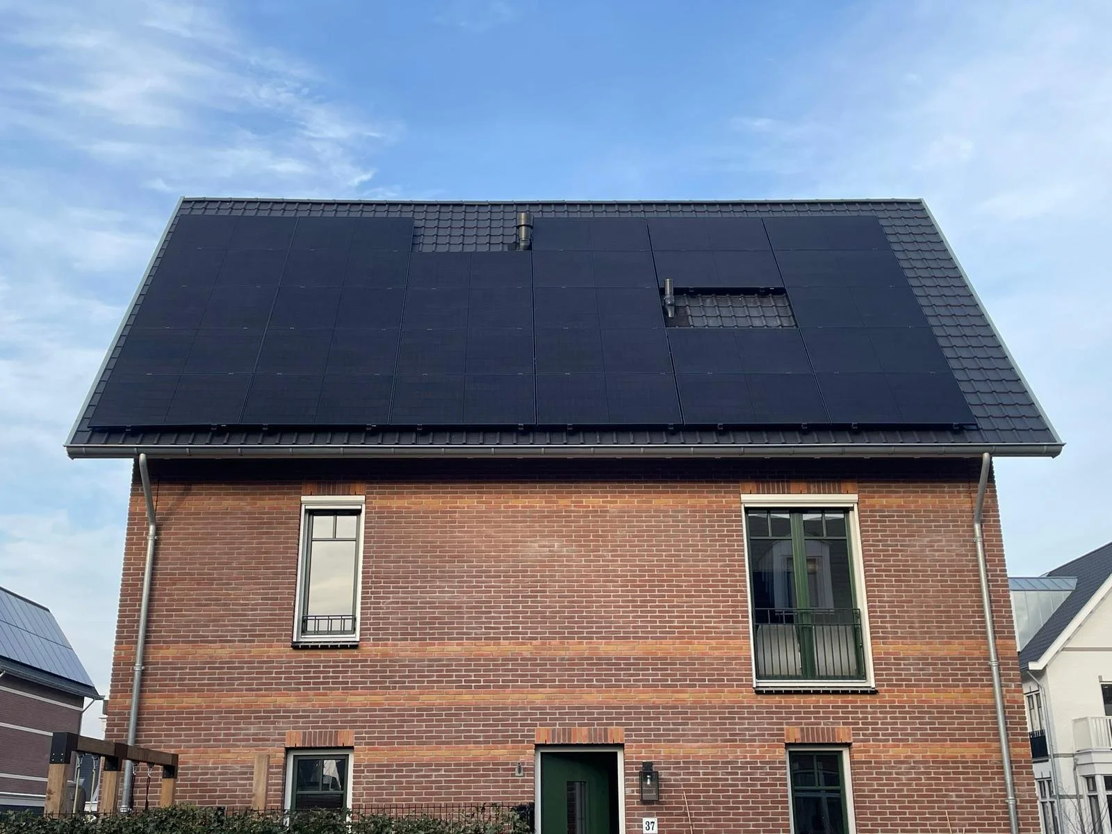 Een huis met zonnepanelen op het dak onder een blauwe lucht met wat wolken.