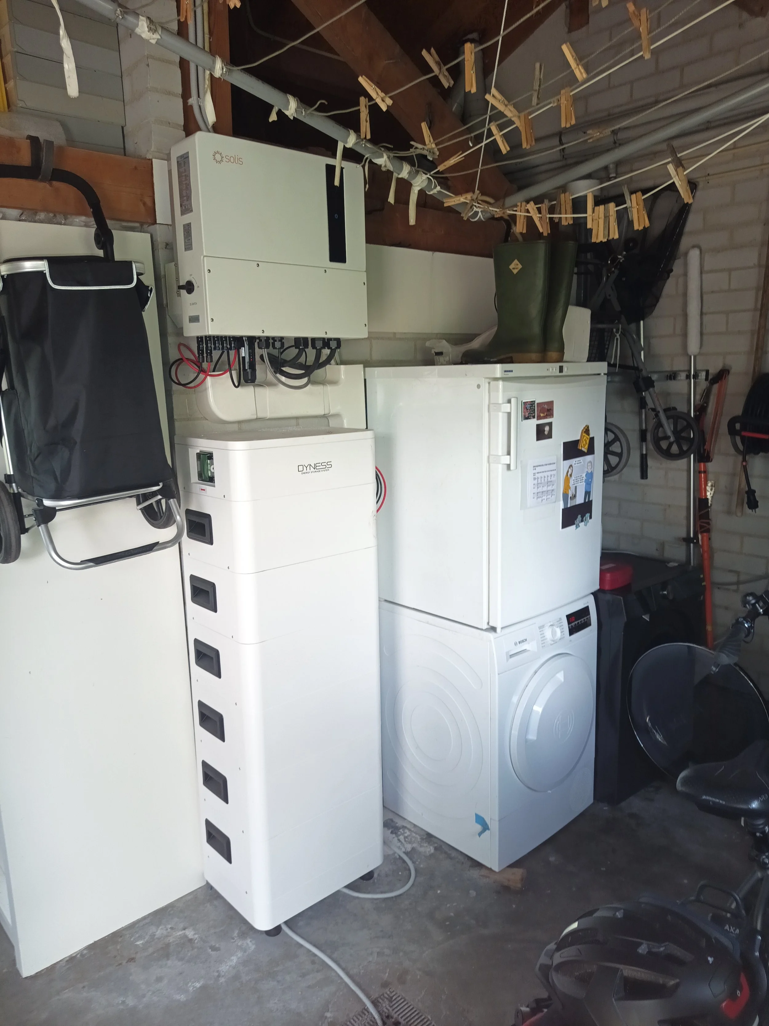 Een ruimte met een wasmachine, een vriezer, een witkast en een boiler. Ook hangen er waslijnen met was en wasknijpers en is er een fiets en een veiligheidslaarzen zichtbaar.