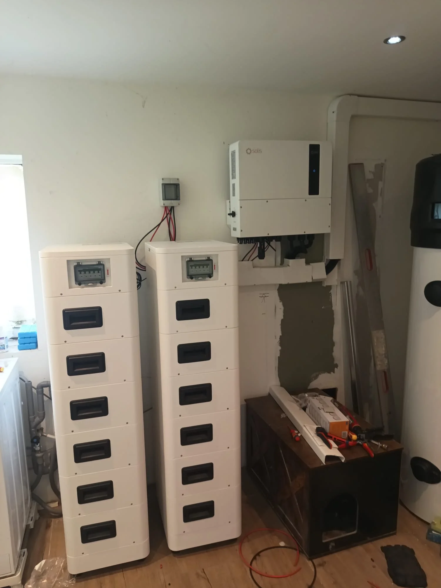 Binnenkant van een techniekkast met zonnepanelen en meetapparatuur, gereedschap, kabellijm en elektrische bedrading.