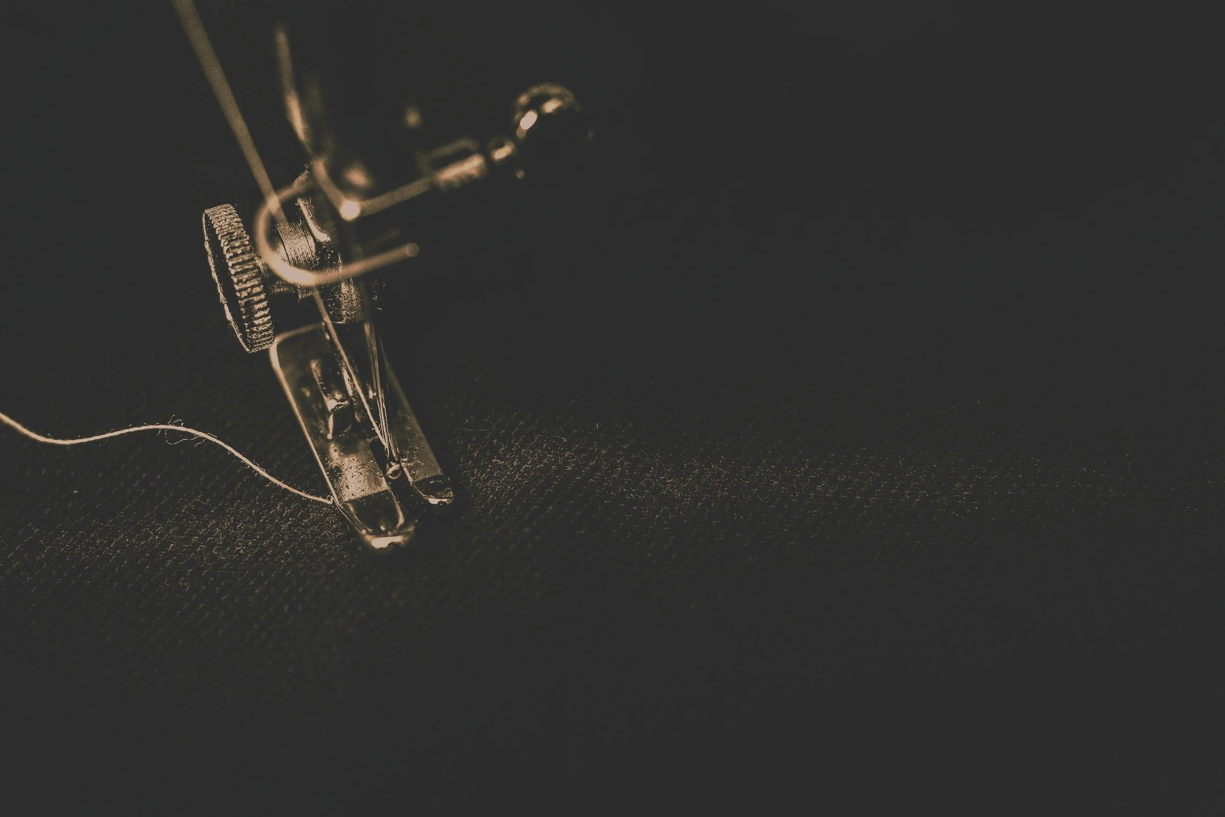 Close-up of a vintage sewing machine needle and mechanisms on a dark background.