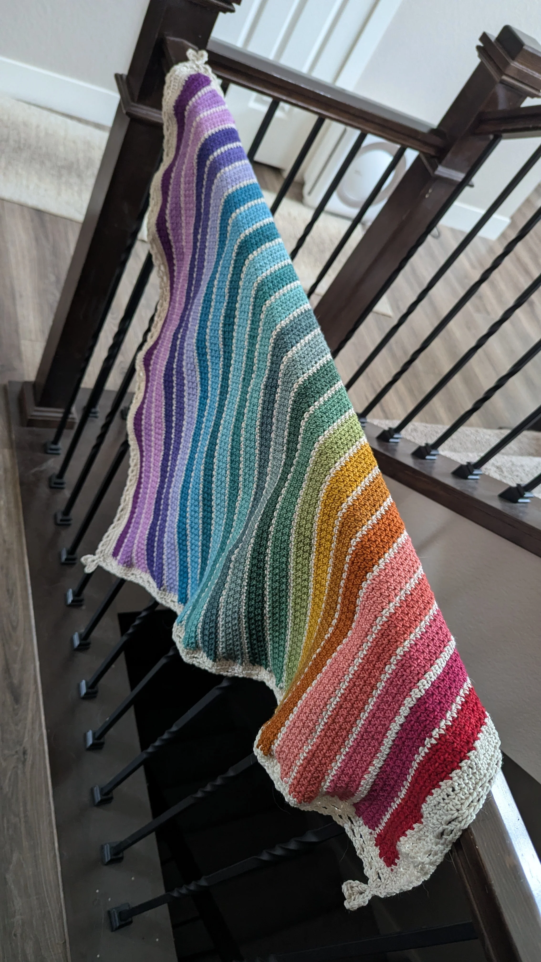 A colorful rainbow-striped knitted blanket draped over a black metal stair railing in a home interior.