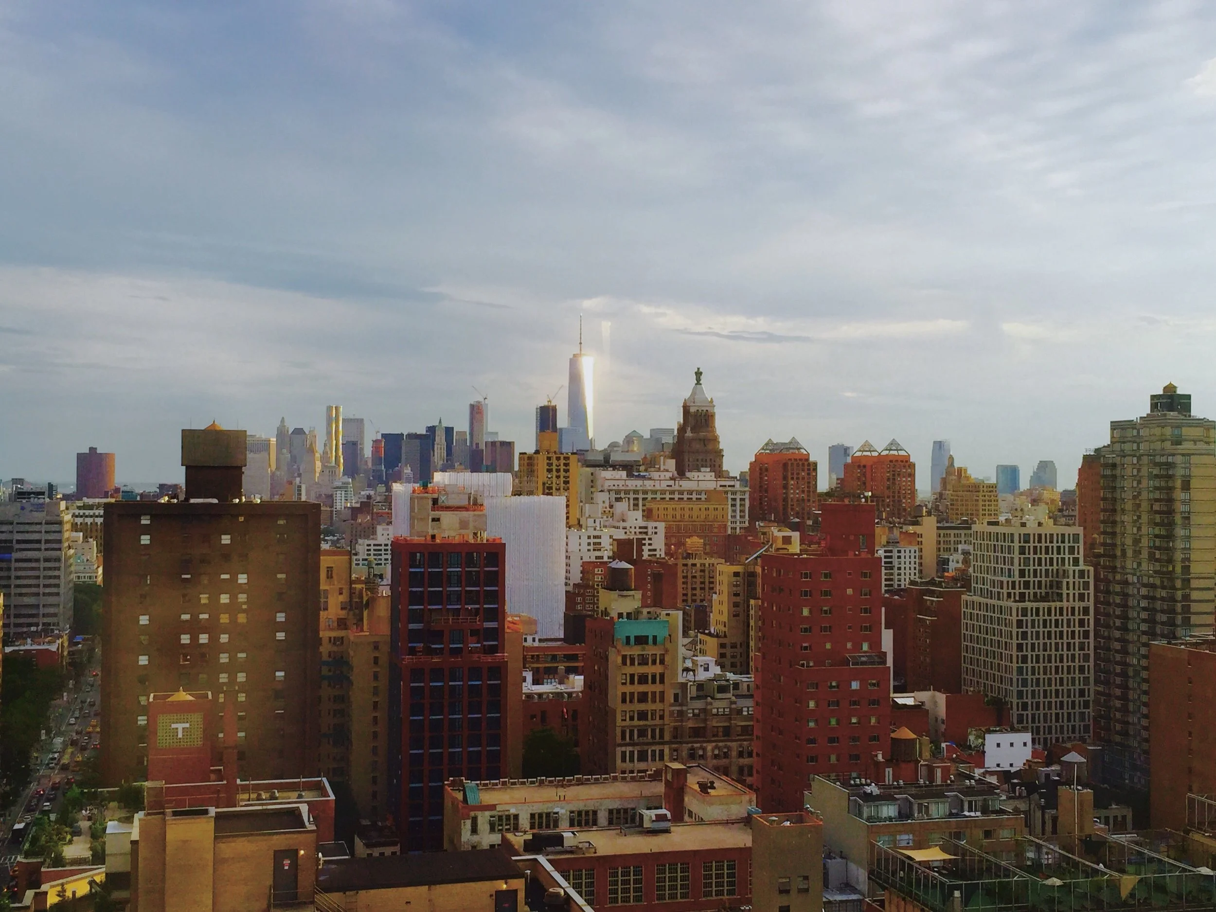 City skyline with various tall buildings, including a prominent tall building with a spire, under a partly cloudy sky.