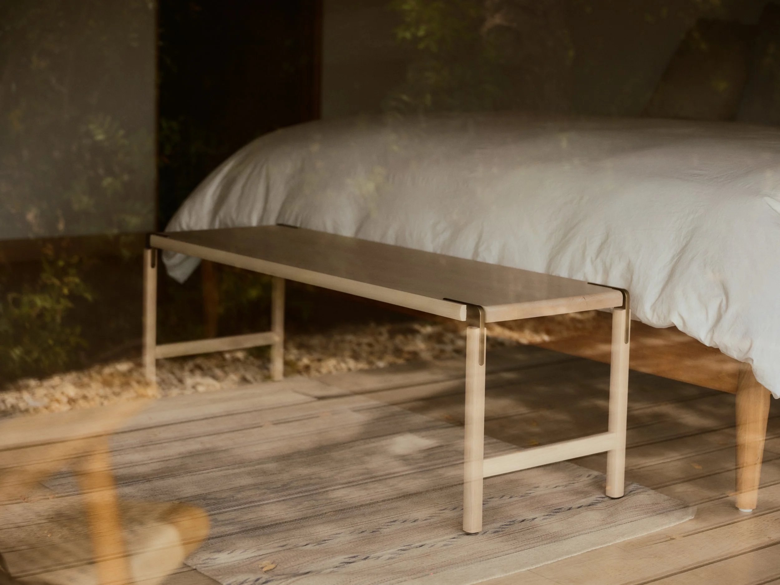 A bed with white linens and a wooden frame, placed on a wooden deck outdoors at night, with blurred golden retriever dog in motion at the bottom left corner.