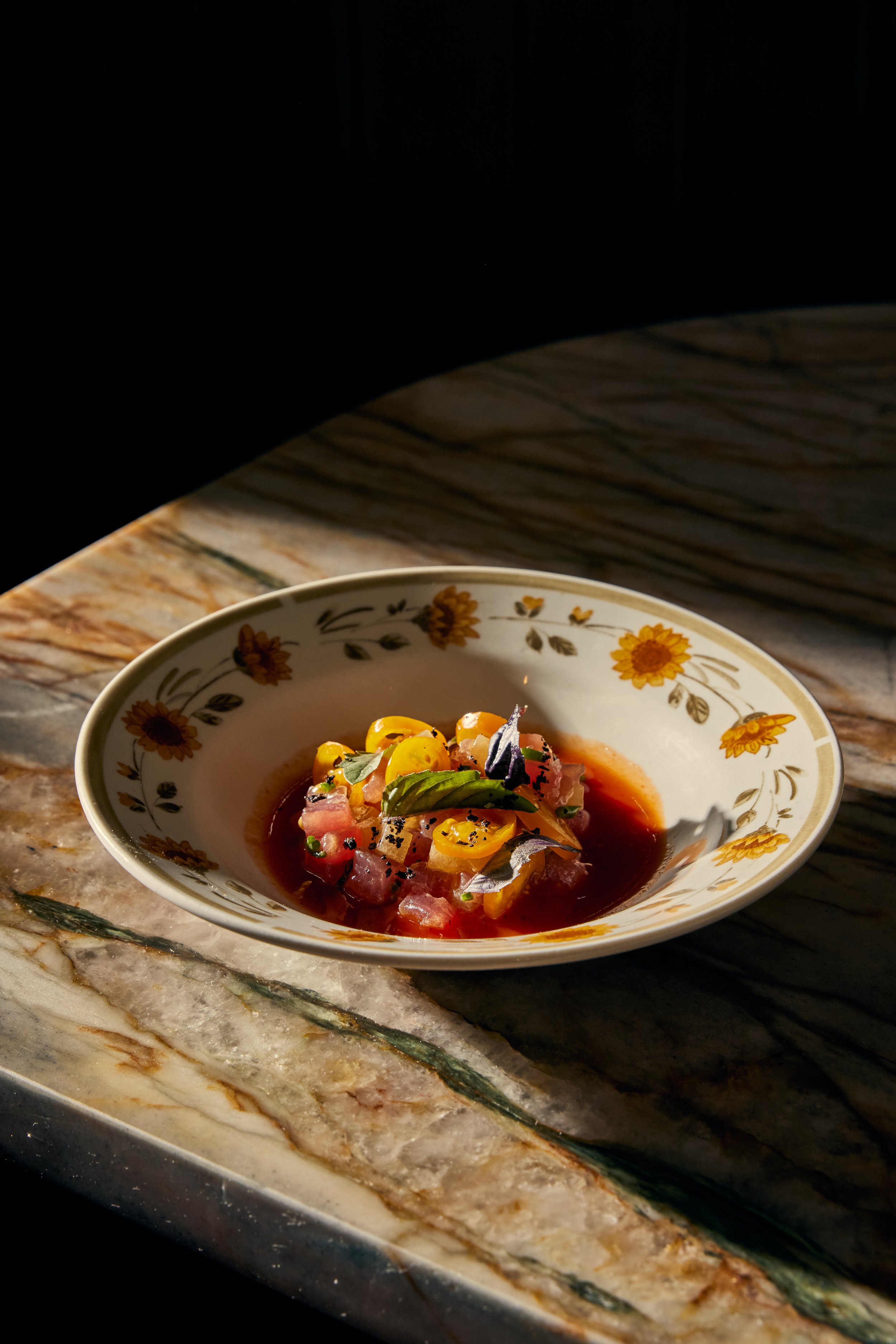 A bowl of ceviche with diced fish, corn, herbs, and black pepper, placed on a wooden surface with a marble countertop nearby.