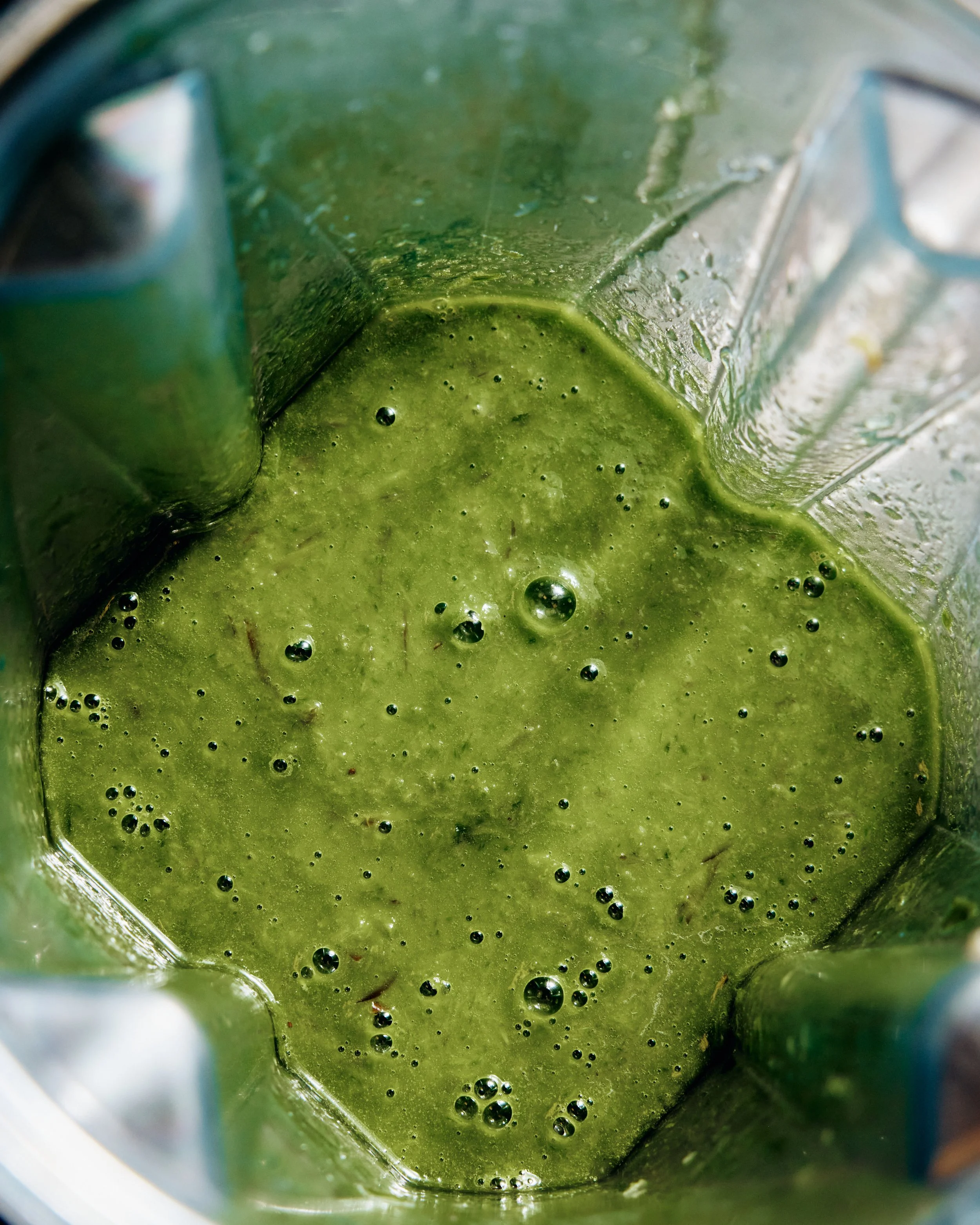 Close-up view of green juice or smoothie with bubbles inside, seen from the top.