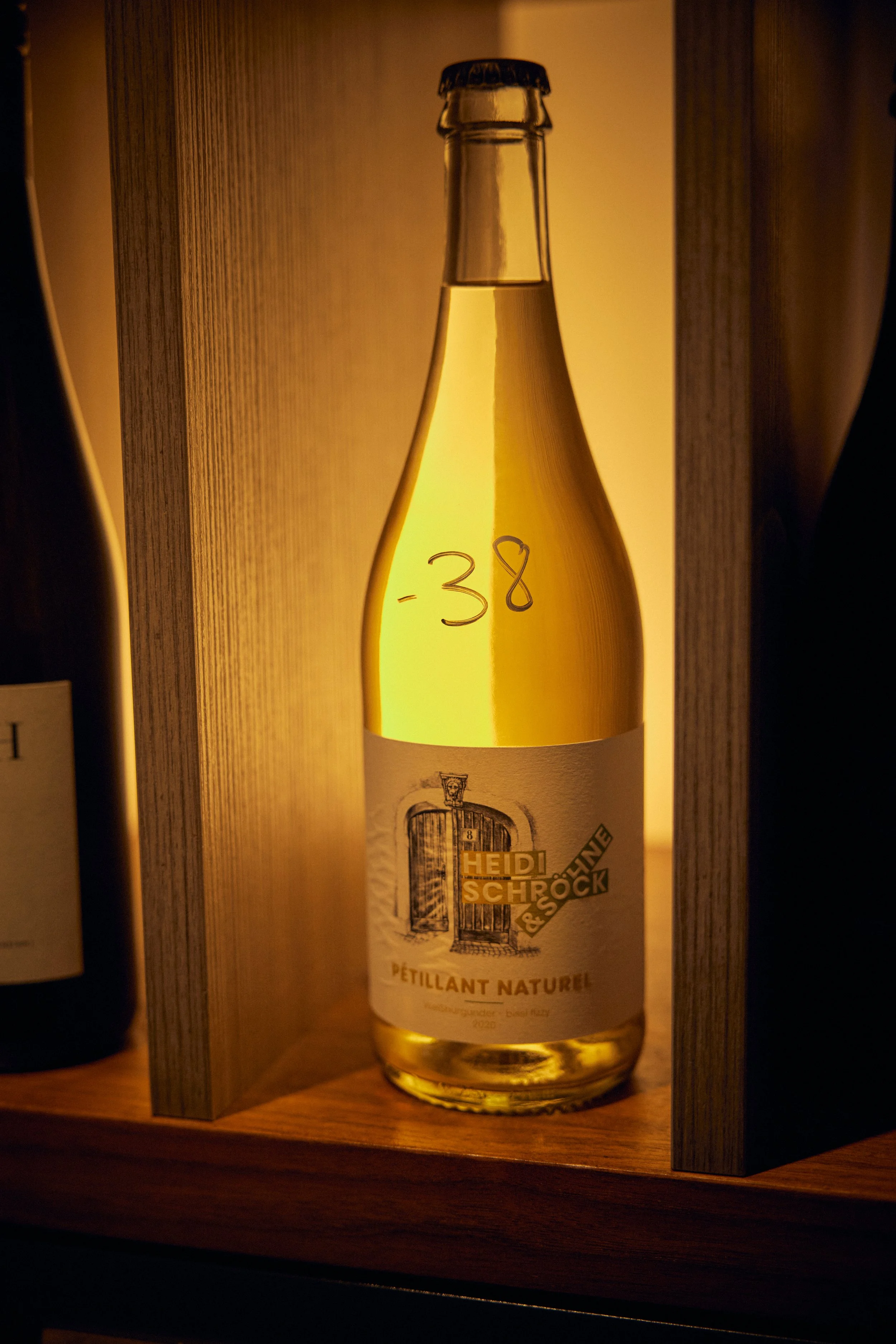 A bottle of sparkling wine with the label reading 'Heidi Schrock', placed inside a wooden box with a warm light illuminating it.