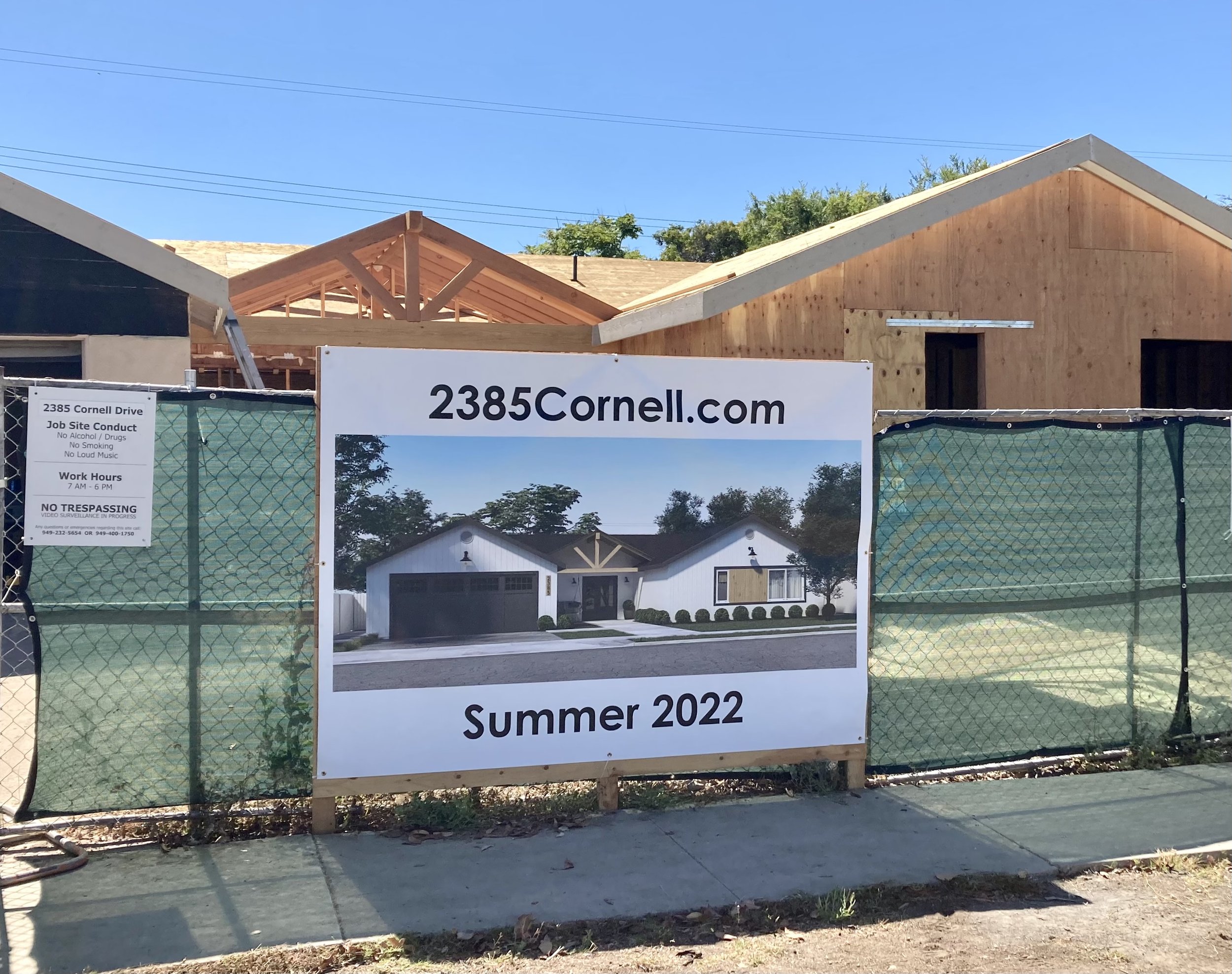 A house under construction with wooden framing, a partially installed roof, and a sign in front that reads '2385 Cornell.com Summer 2022'.