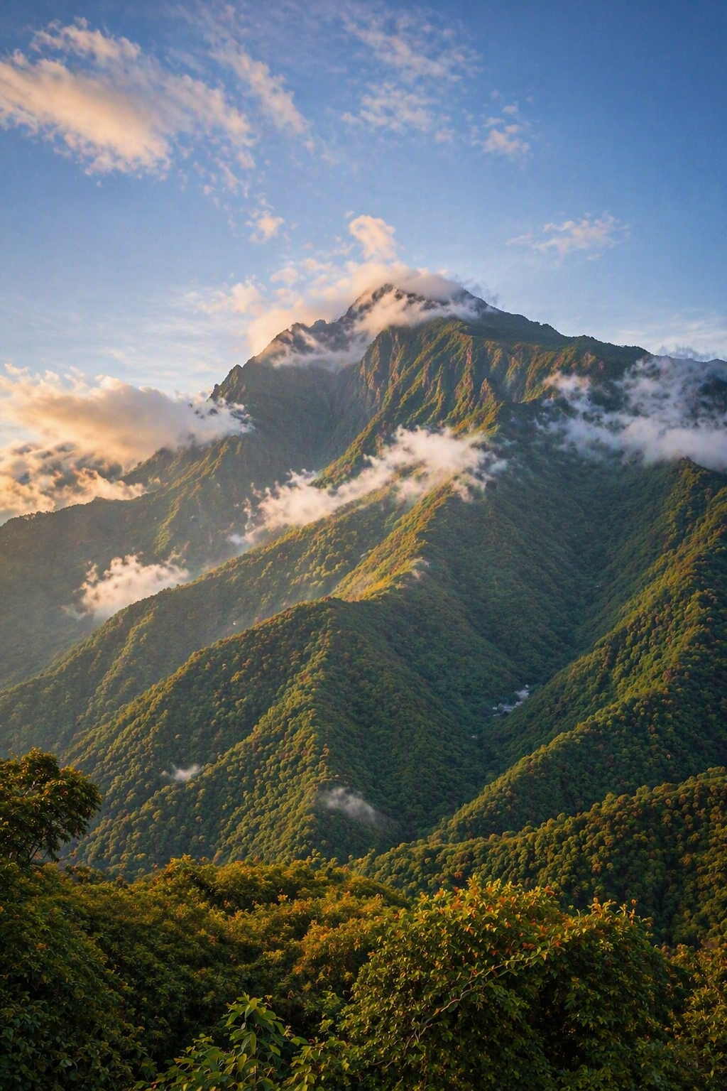 A lush green mountain landscape with clouds surrounding the peaks and a partly cloudy sky.