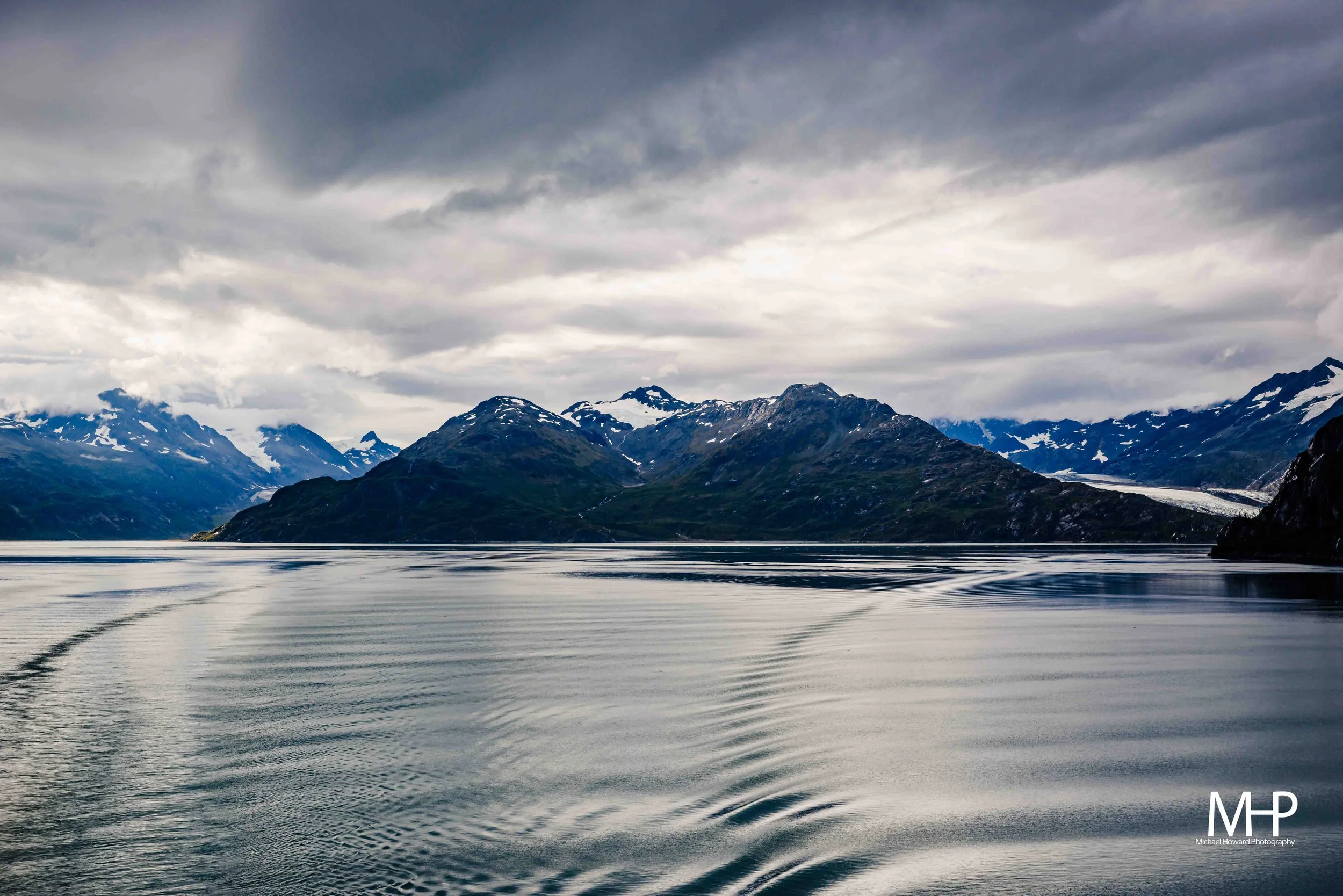 A scenic view of snow-capped mountains across a body of water under cloudy sky.