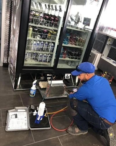 Technicien effectuant une maintenance sur un réfrigérateur commercial dans un magasin.