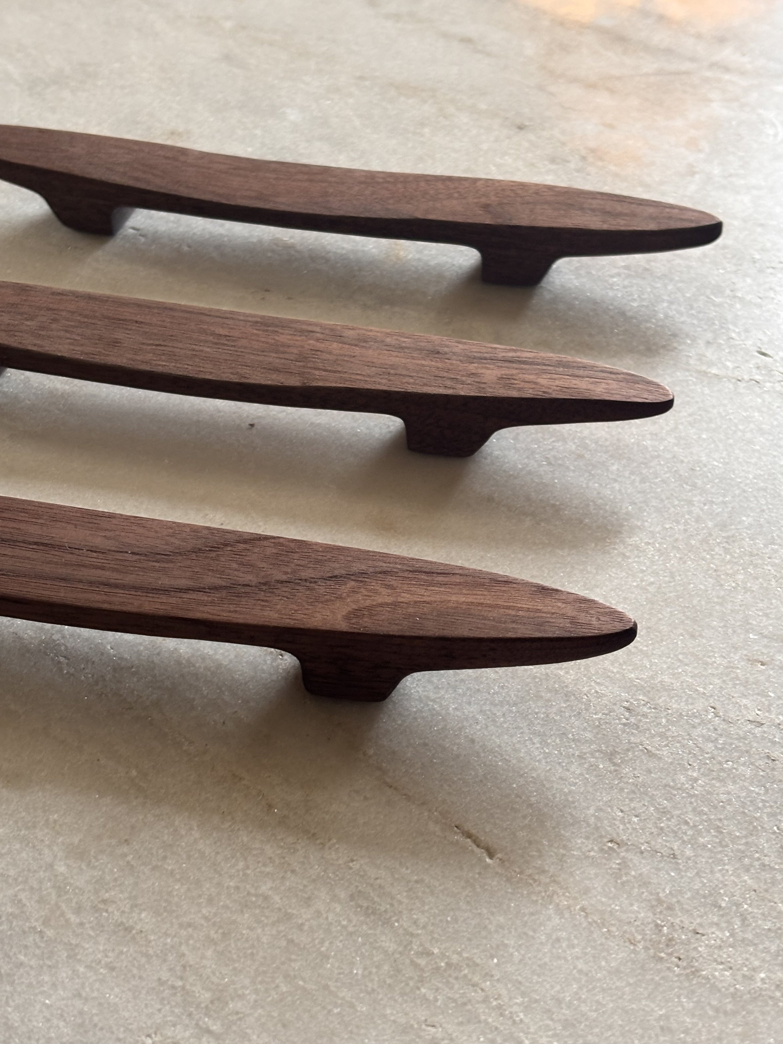 Close-up of three wooden drawer handles on a light-colored surface.