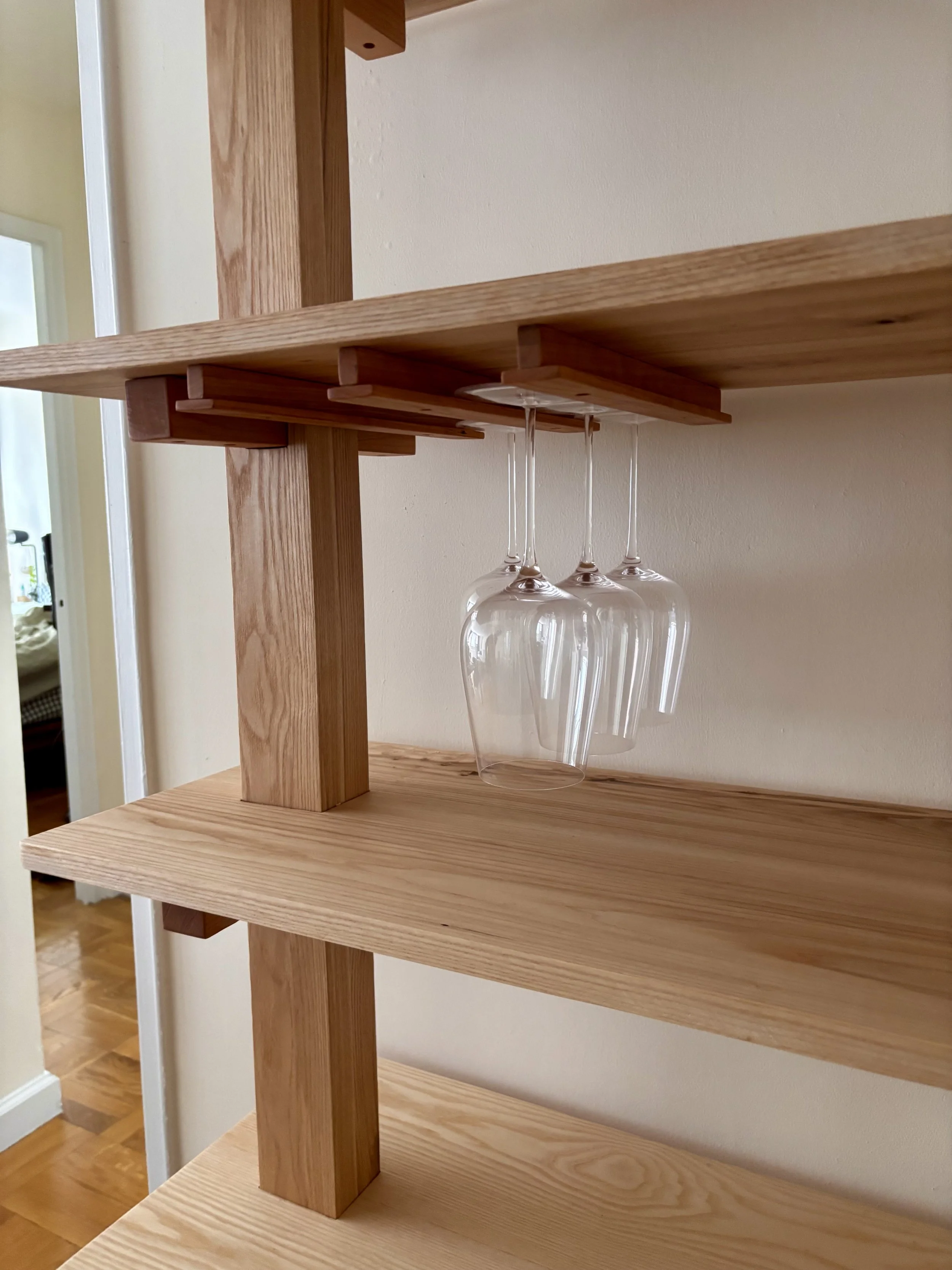 A japandi-style wooden shelf with a cherry wood glass holder showing three upside-down wine glasses hanging underneath on a horizontal shelf.