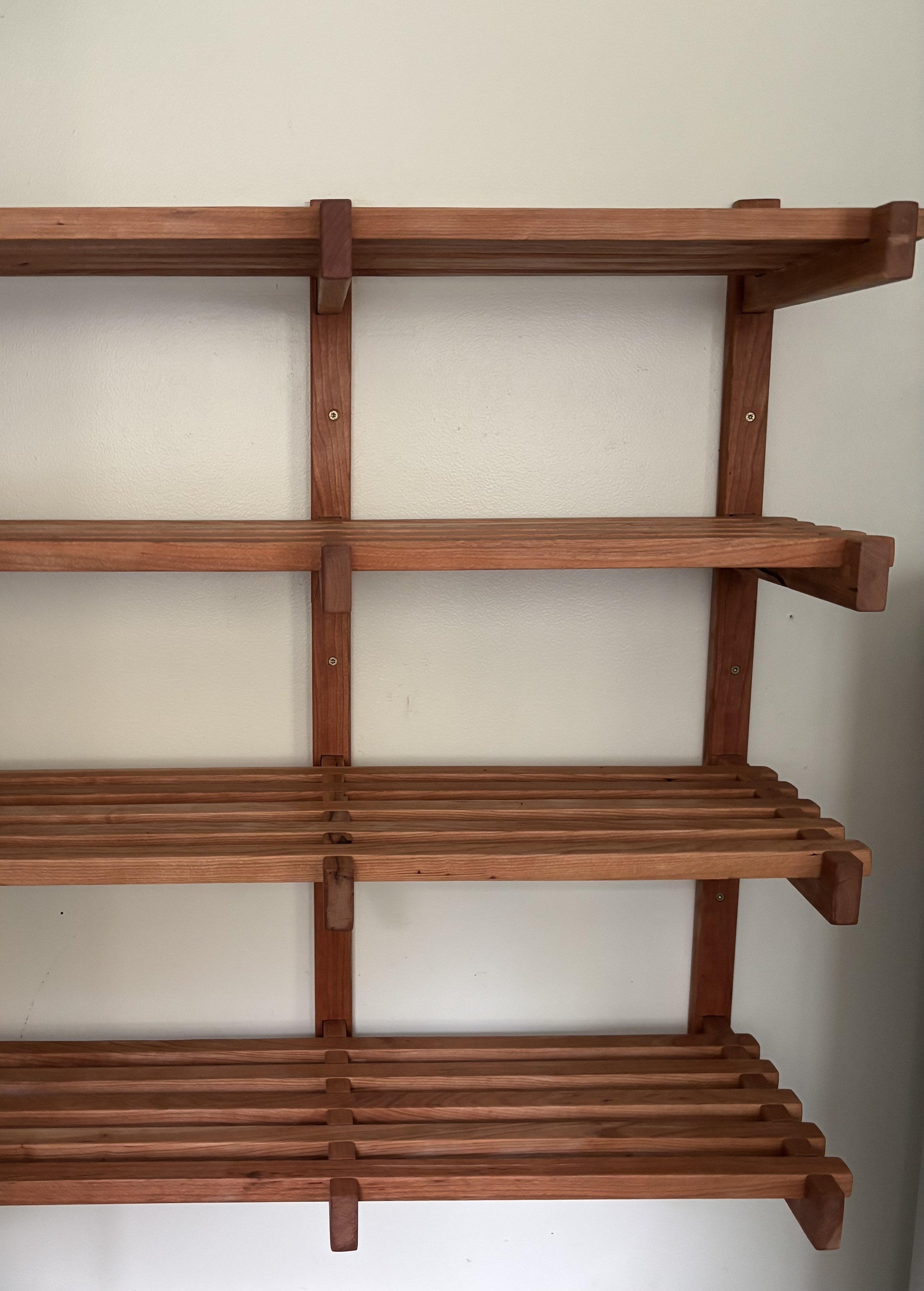 A modern Scandinavian style cherry wood shelving unit with multiple tiers of shelves in a entry room