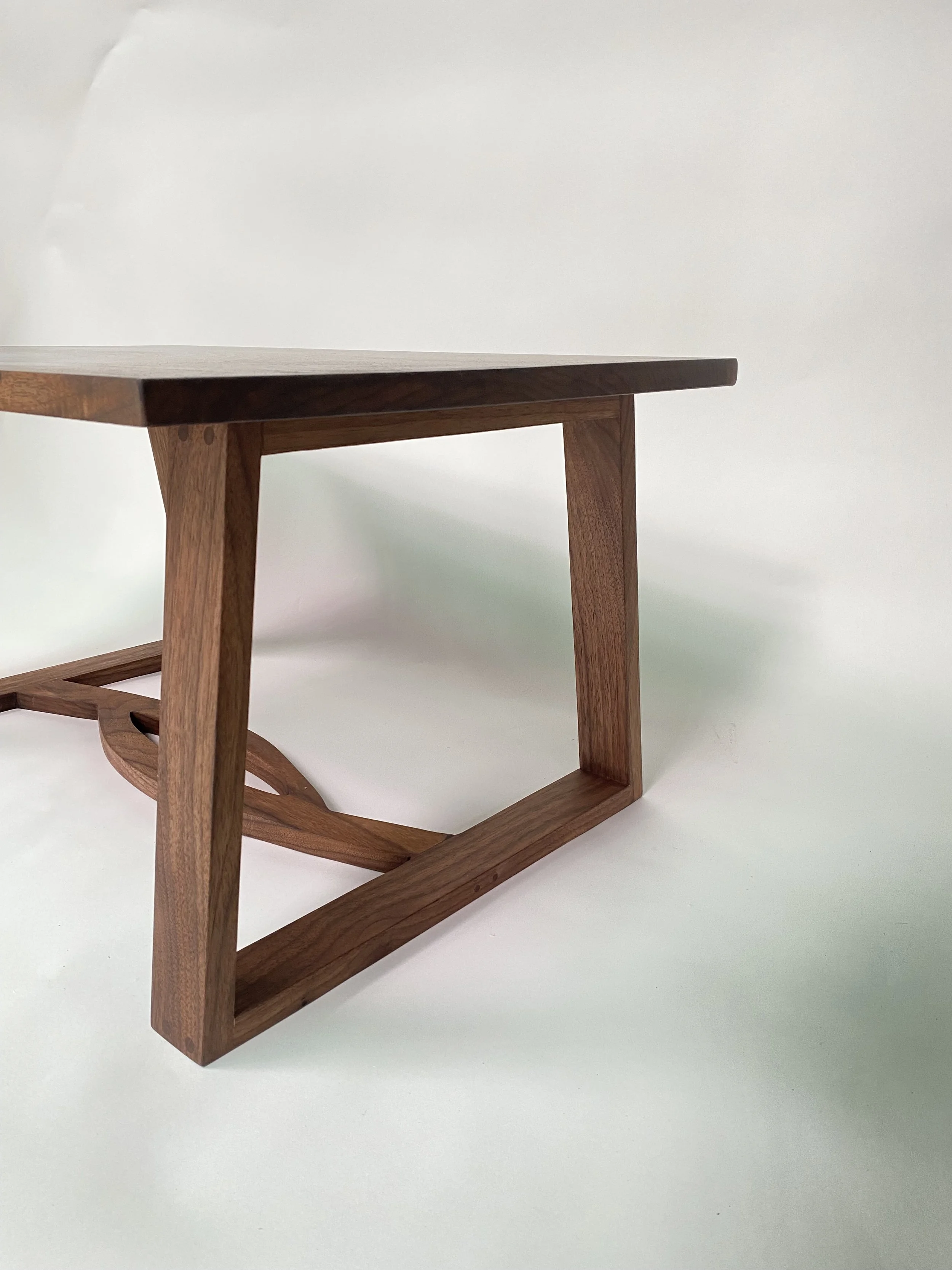 Wooden walnut coffee table with a simple rectangular top and a geometric open-frame base.