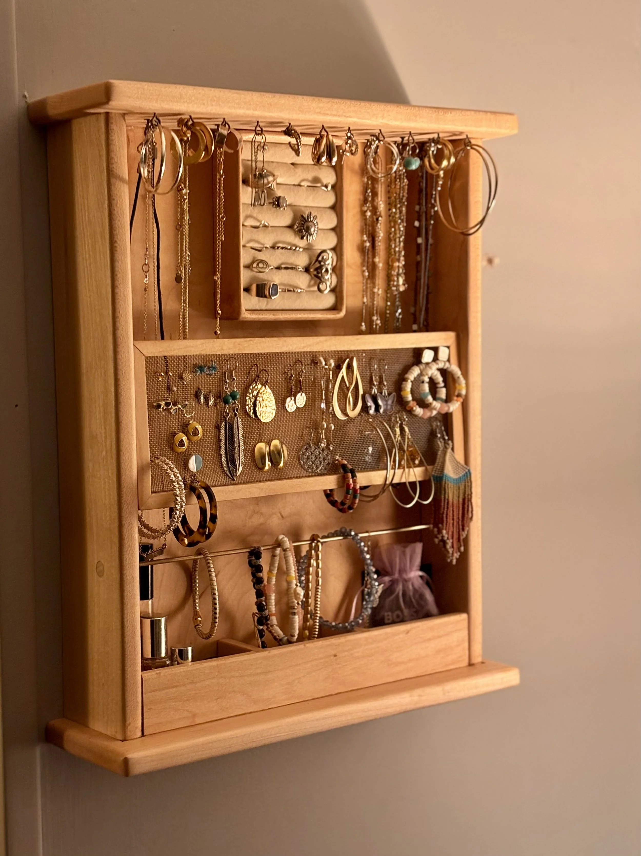 A wooden jewelry display shelf with various necklaces, earrings, and rings hanging on hooks and laid out on shelves.