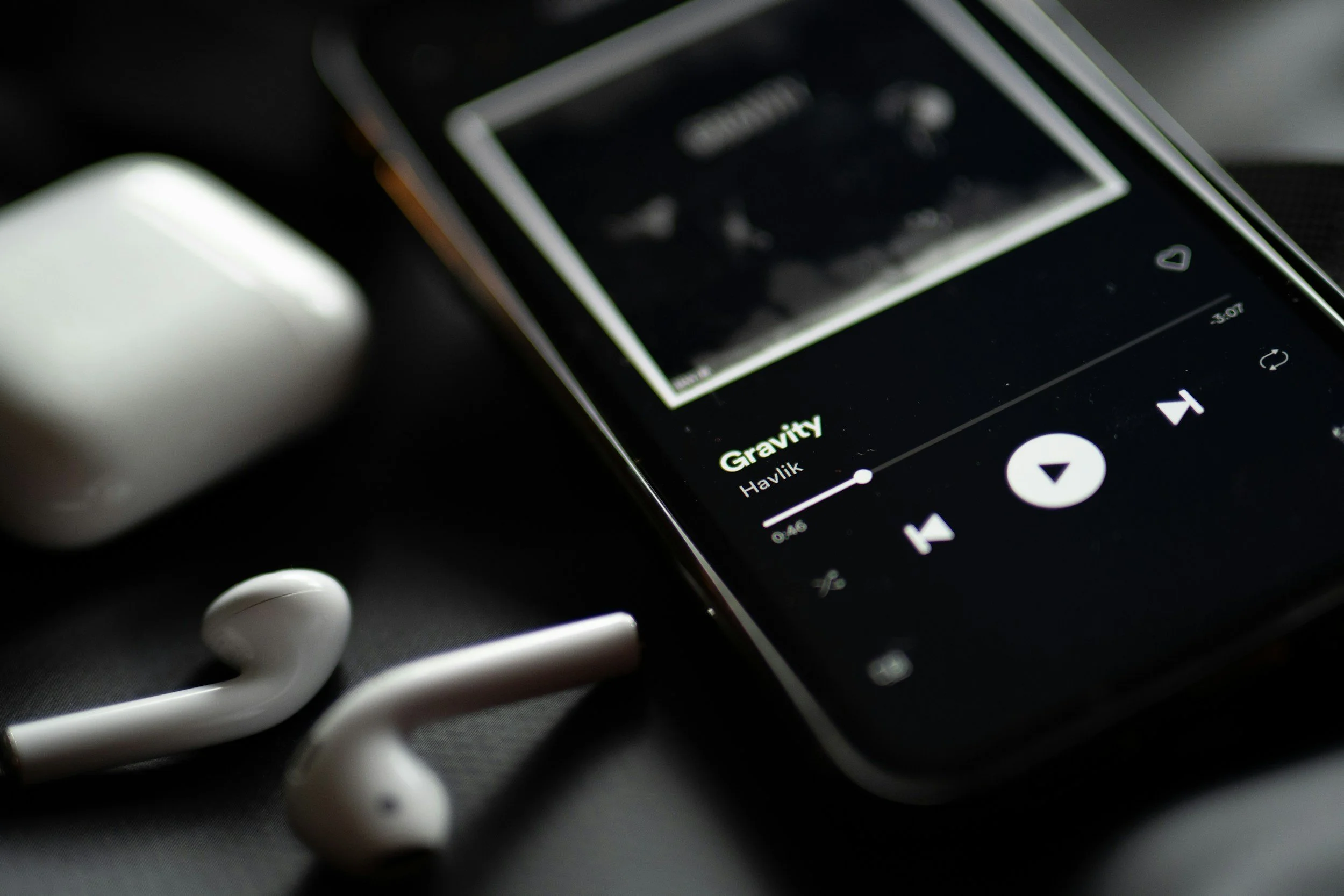 Close-up of a smartphone playing song 'Gravity' by Havik, with white earphones resting nearby.