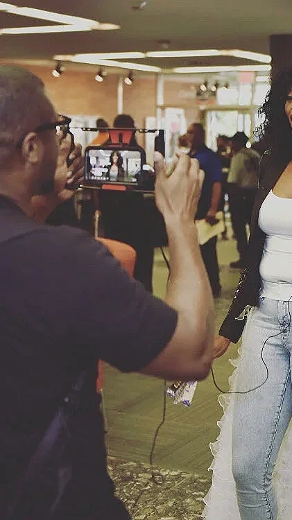 A man taking a photo of a woman with a smartphone in an indoor setting, possibly at an event or gathering.