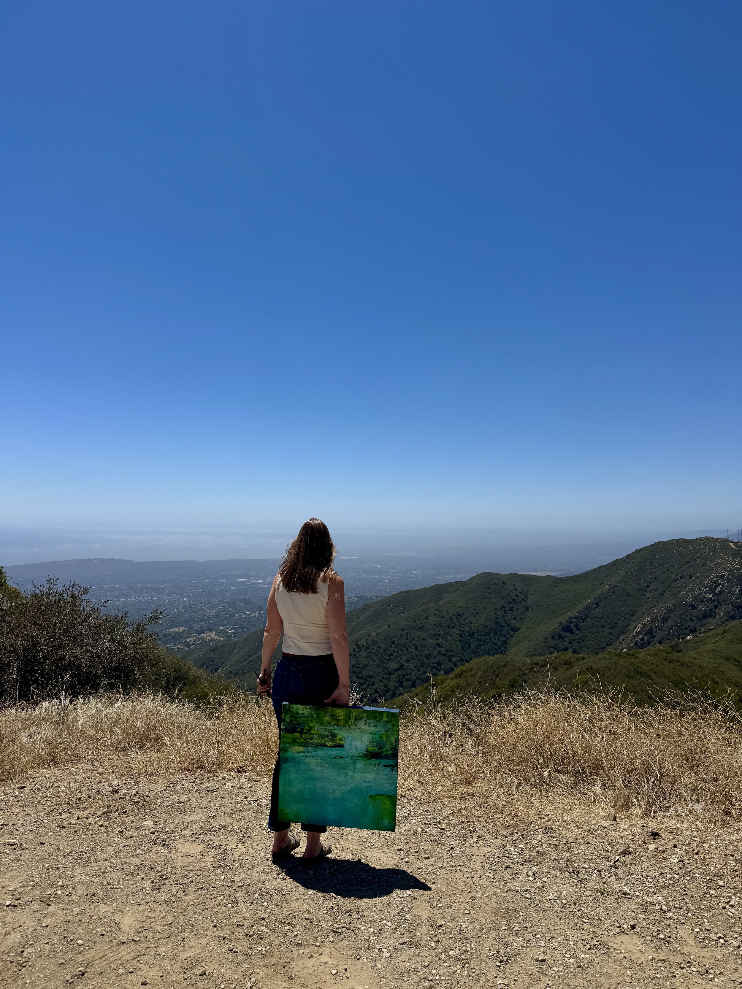 Kristen Wagner holding an original abstract painting in a Santa Barbara landscape.