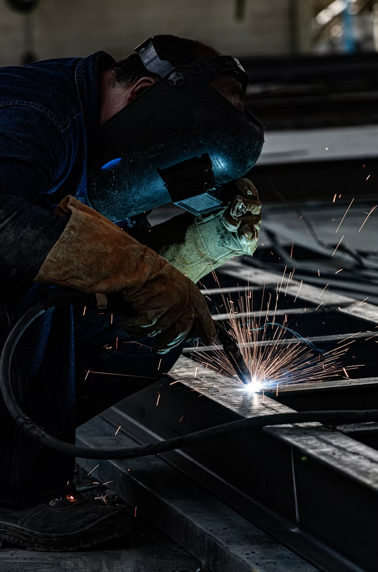 A worker welding metal beams with sparks flying in a workshop.