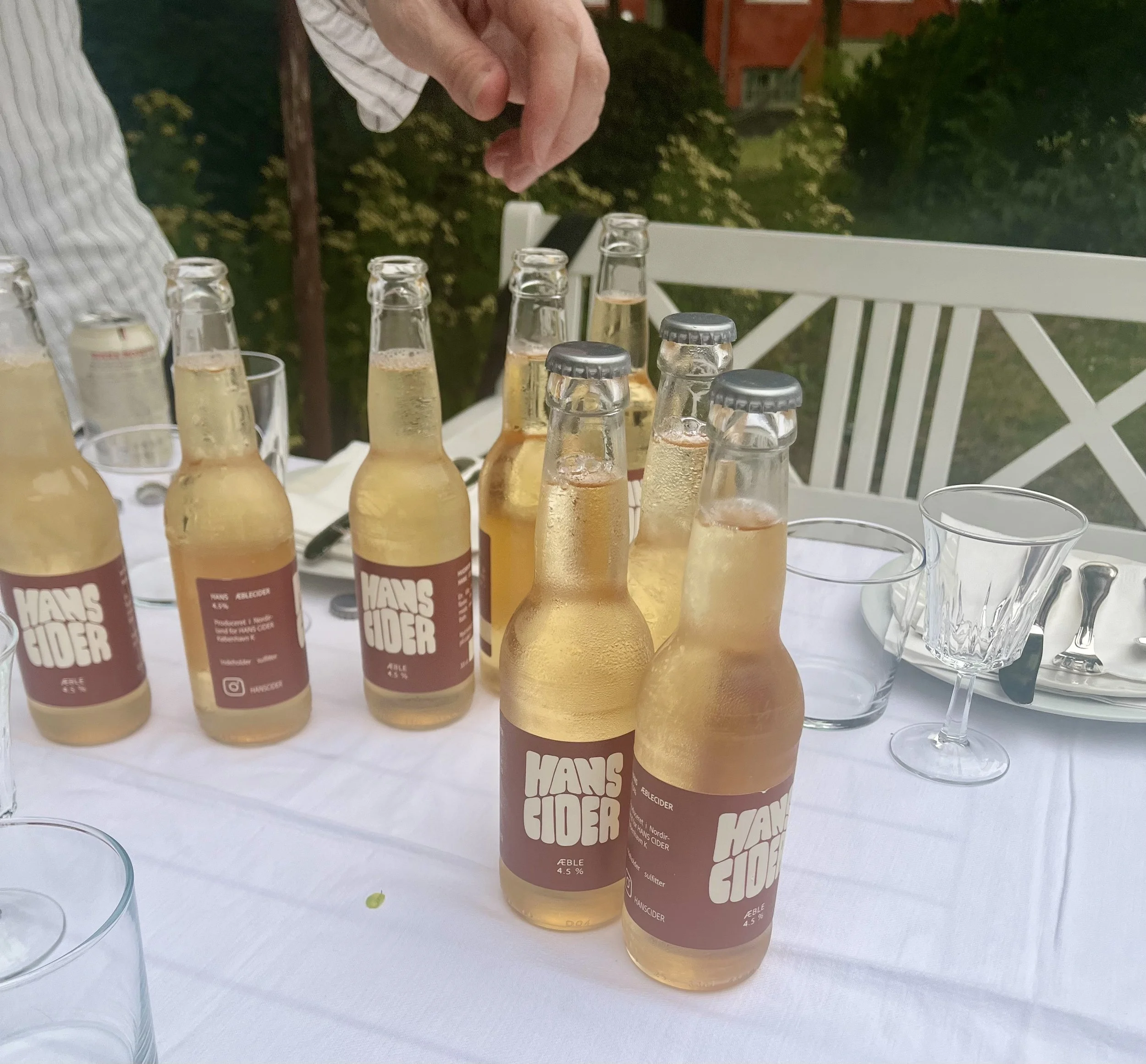 Flere glas med lyserød/gylden alkoholholdig drik og flasker med øl på en hvid dug, omgivet af glas og partydimser.