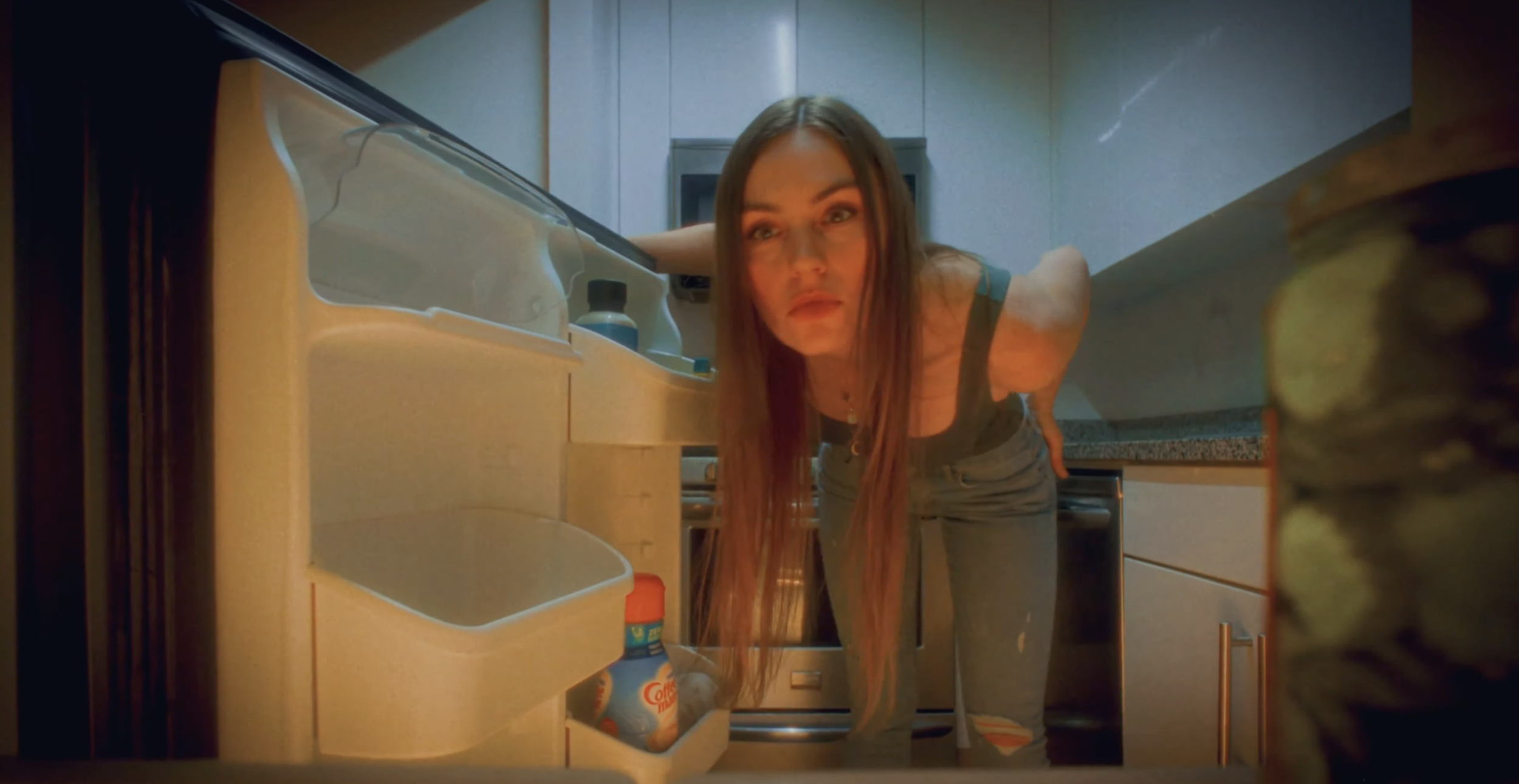 A woman with long hair leaning into an open refrigerator, looking inside it in a kitchen.