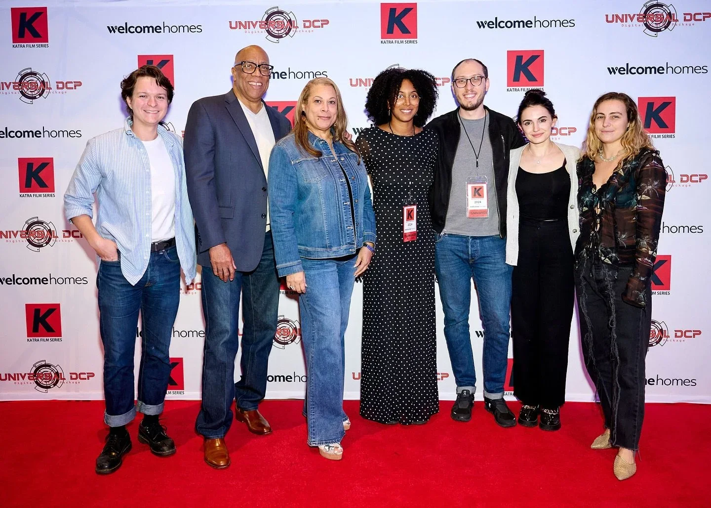 Group of seven people standing on a red carpet at an event, with a backdrop featuring logos of 'Universal DCP', 'welcomehomes', and 'Katra Film Series'.