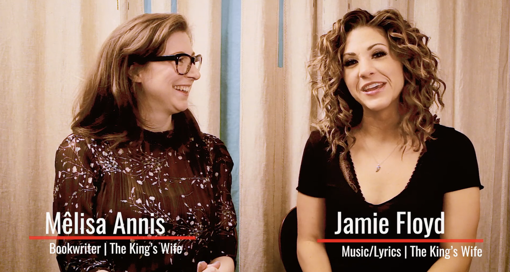 Two women sitting and talking in front of a curtain. The woman on the left has brown hair, glasses, and is wearing a floral blouse. The woman on the right has curly hair and is wearing a black top. Text on the image identifies them as Mêlisa Annis and Jamie Floyd, with their roles as bookwriter and music/lyrics writer for "The King's Wife."